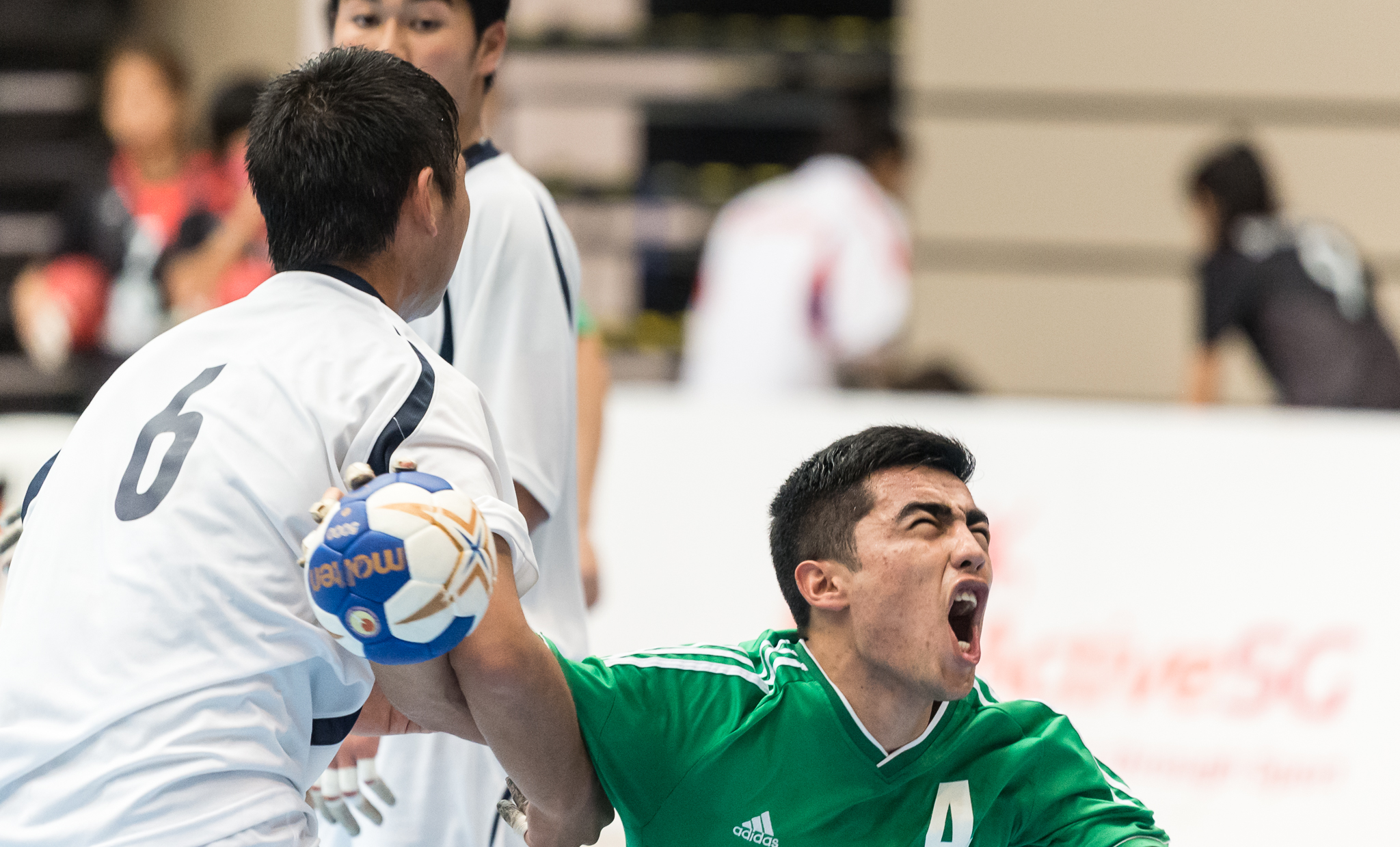 A Japanese player grabs an Uzbek player's arm during an International hand ball match at Our Tampines Hub.