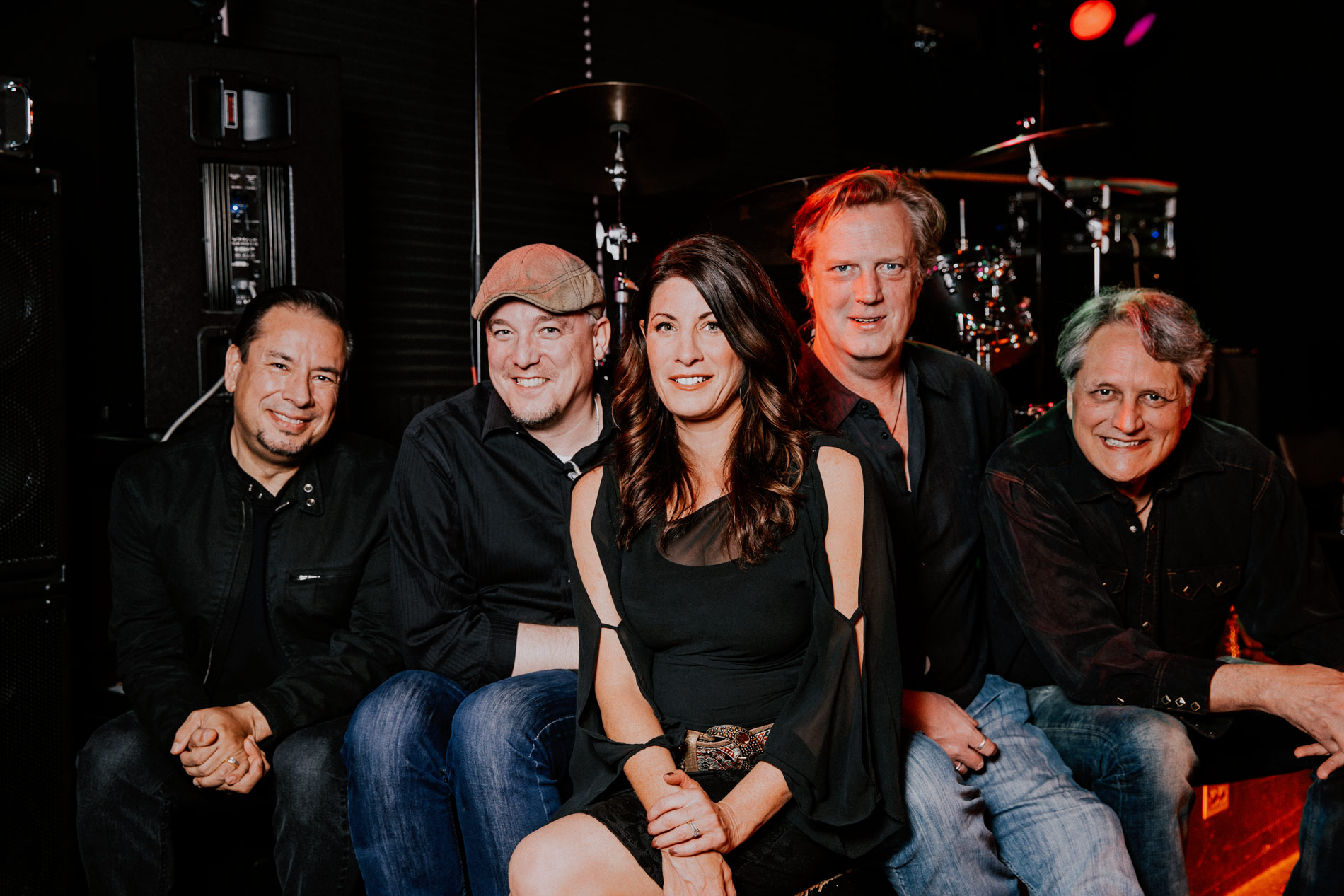 Four men, one woman band sitting on stage, smiling