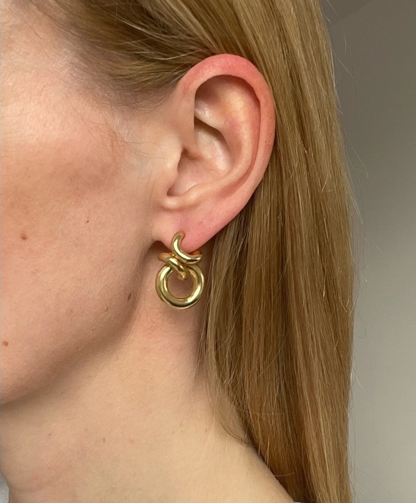 a close up of a models ear wearing chunky gold 80's style hoop earrings
