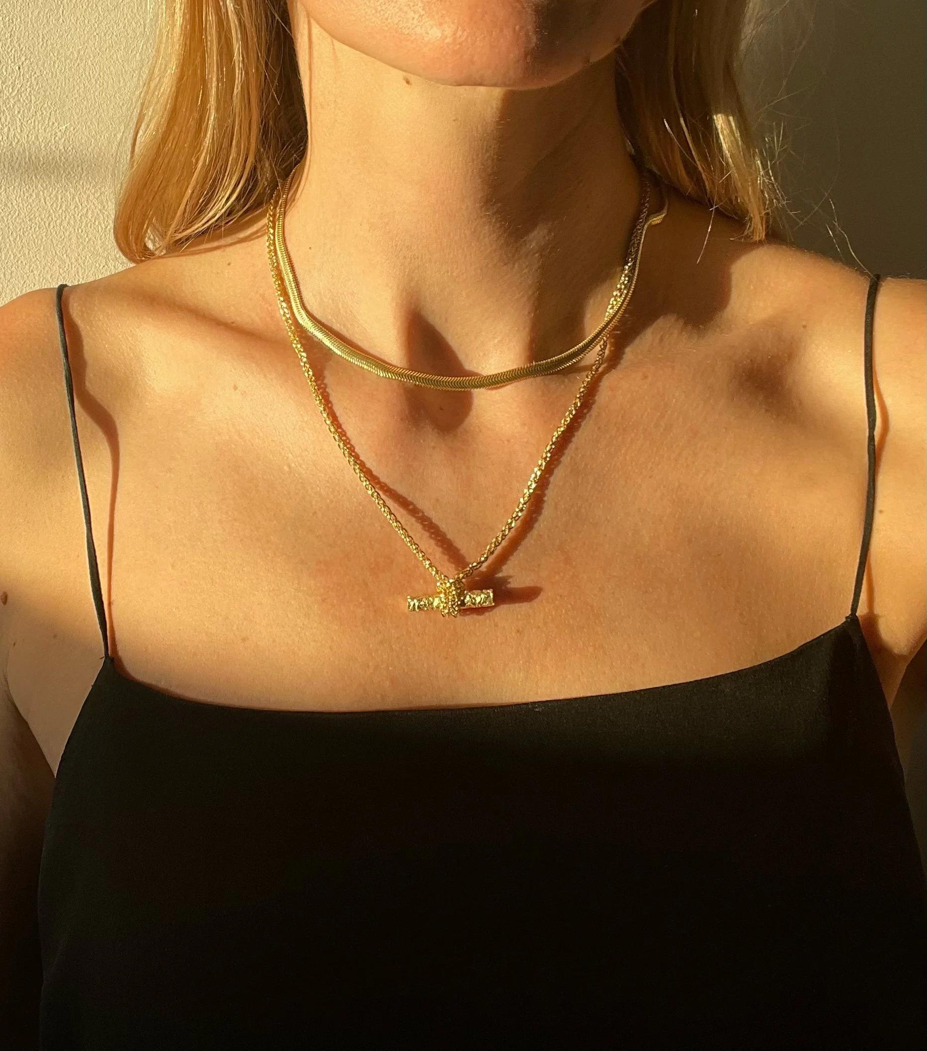 A model wearing a gold flat snake chain and a classic t bar necklace