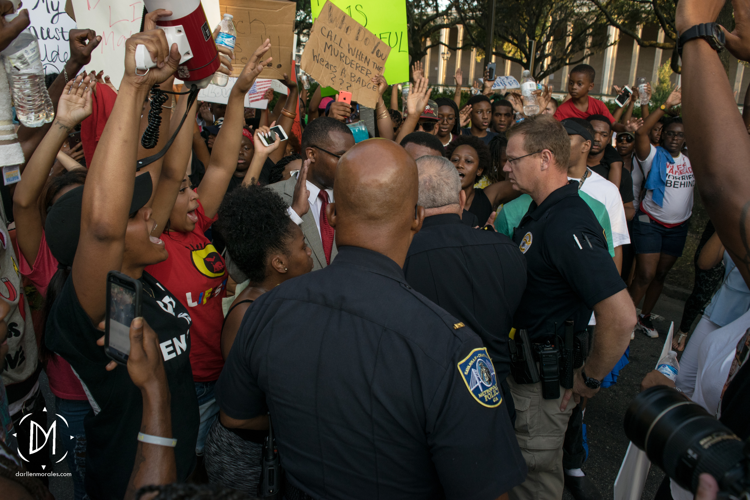      Activists shout, "Hands up, don't shoot" as police officers approach local pastor, Jomo Johnson to discuss the march's route.  &nbsp;  