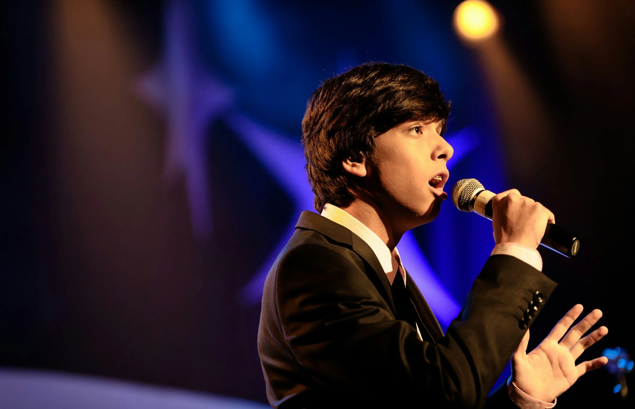 Young boy on stage singing into a microphone