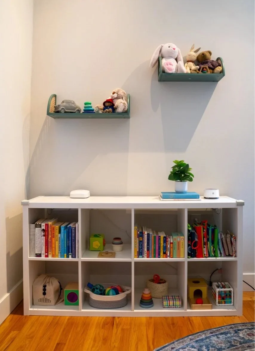 Shelving unit in young kid's bedroom, organized with toys and books. Two floating shelves mounted on wall above with sentimental items.