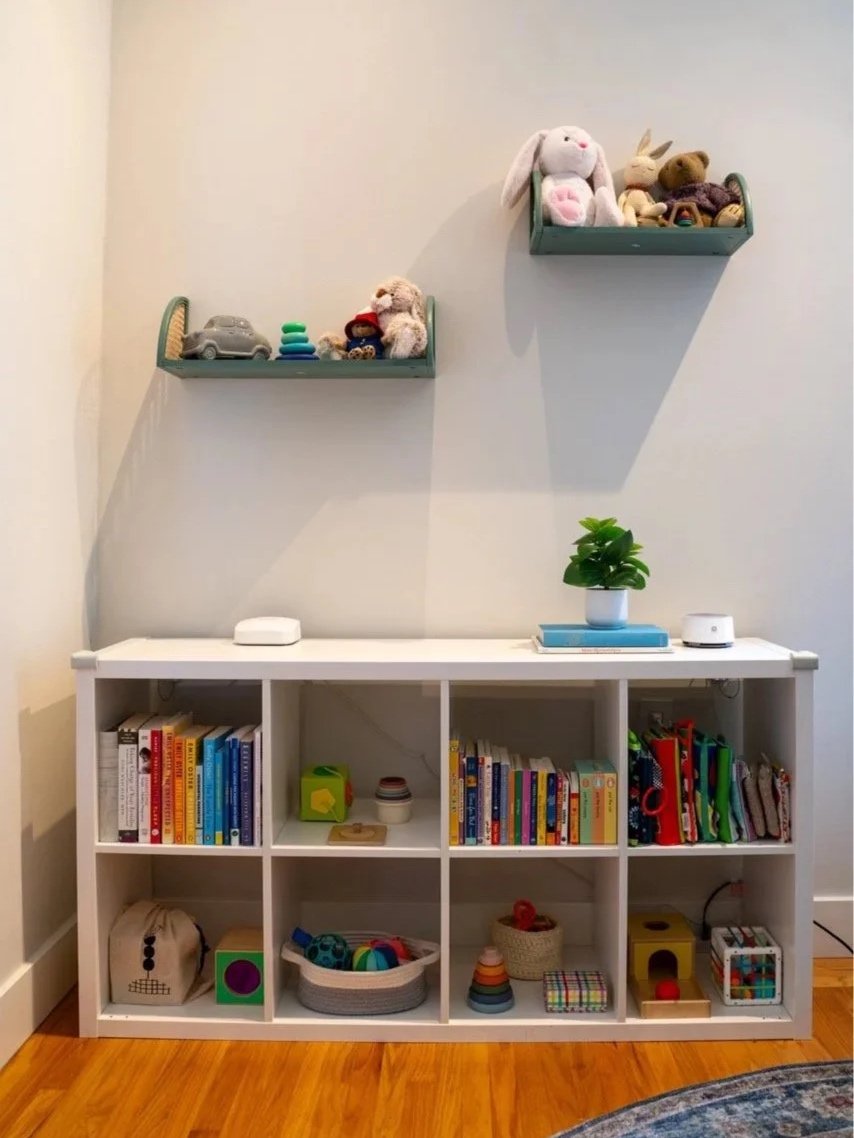 Shelving unit in young kid's bedroom, organized with toys and books. Two floating shelves mounted on wall above with sentimental items.