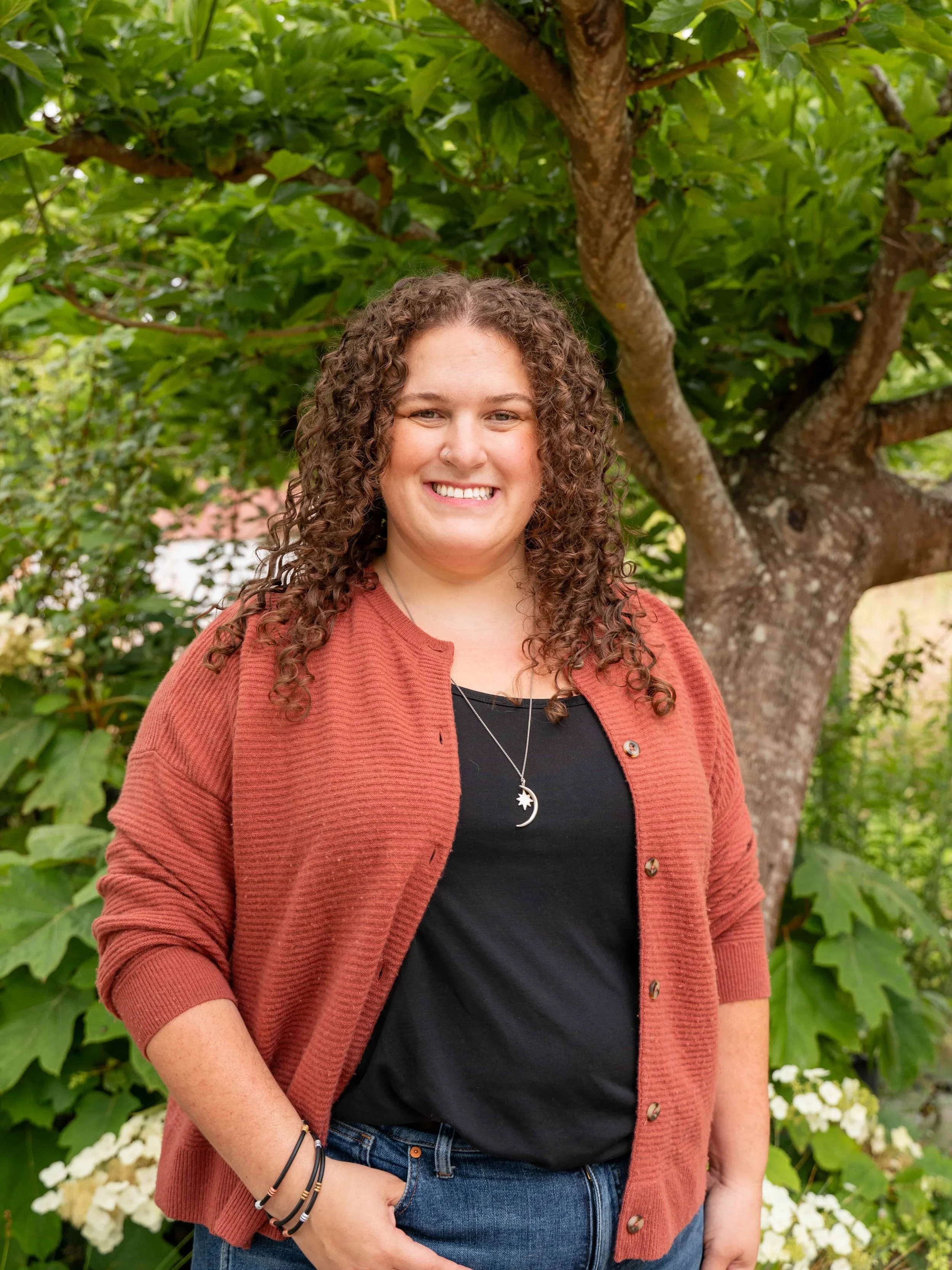 Hannah Gradjansky, designer and organizer, stands in front of green tree