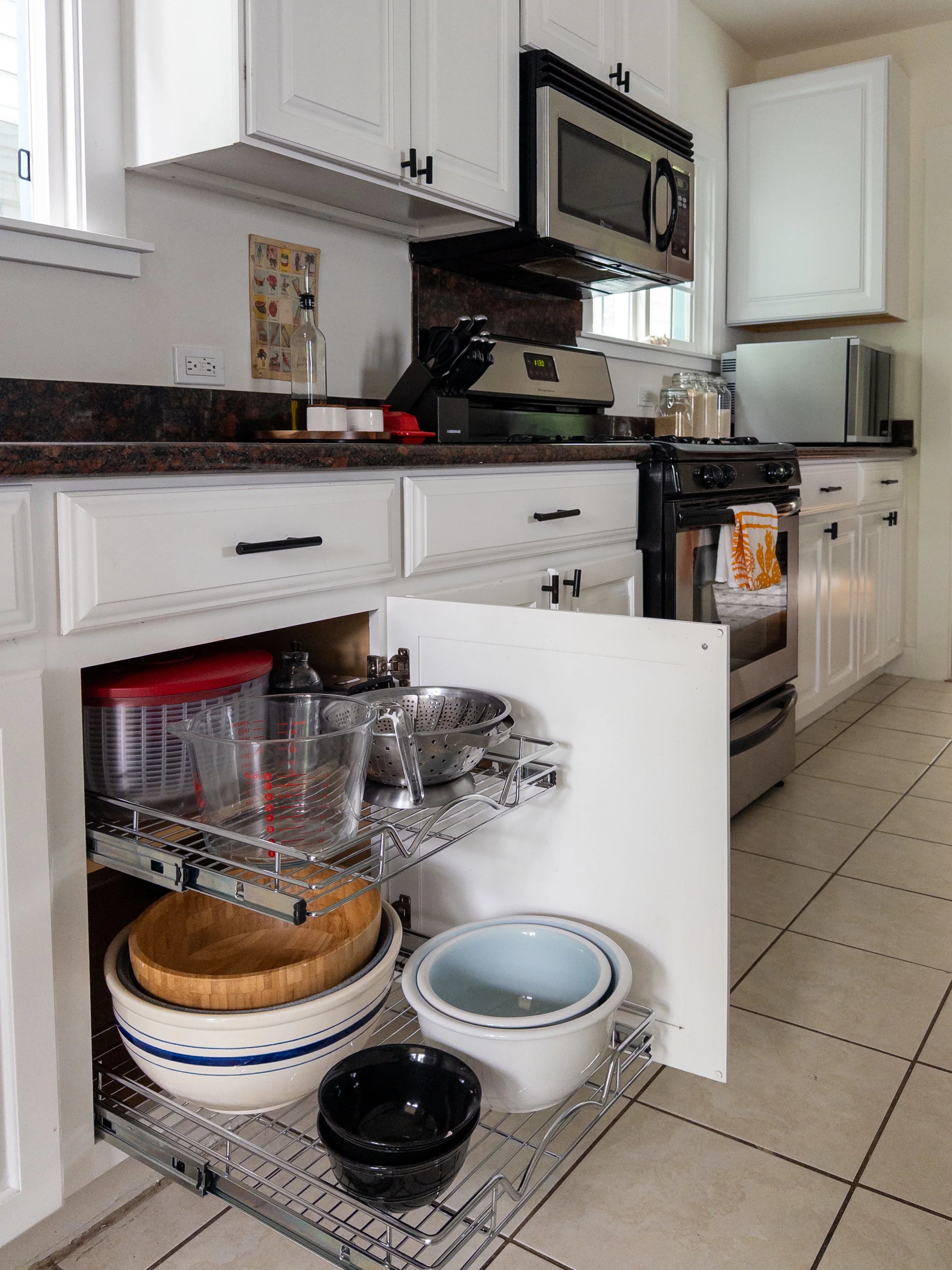 Kitchen Cabinet open to show two newly installed pullout shelves with bowls and cooking tools that improves organization.