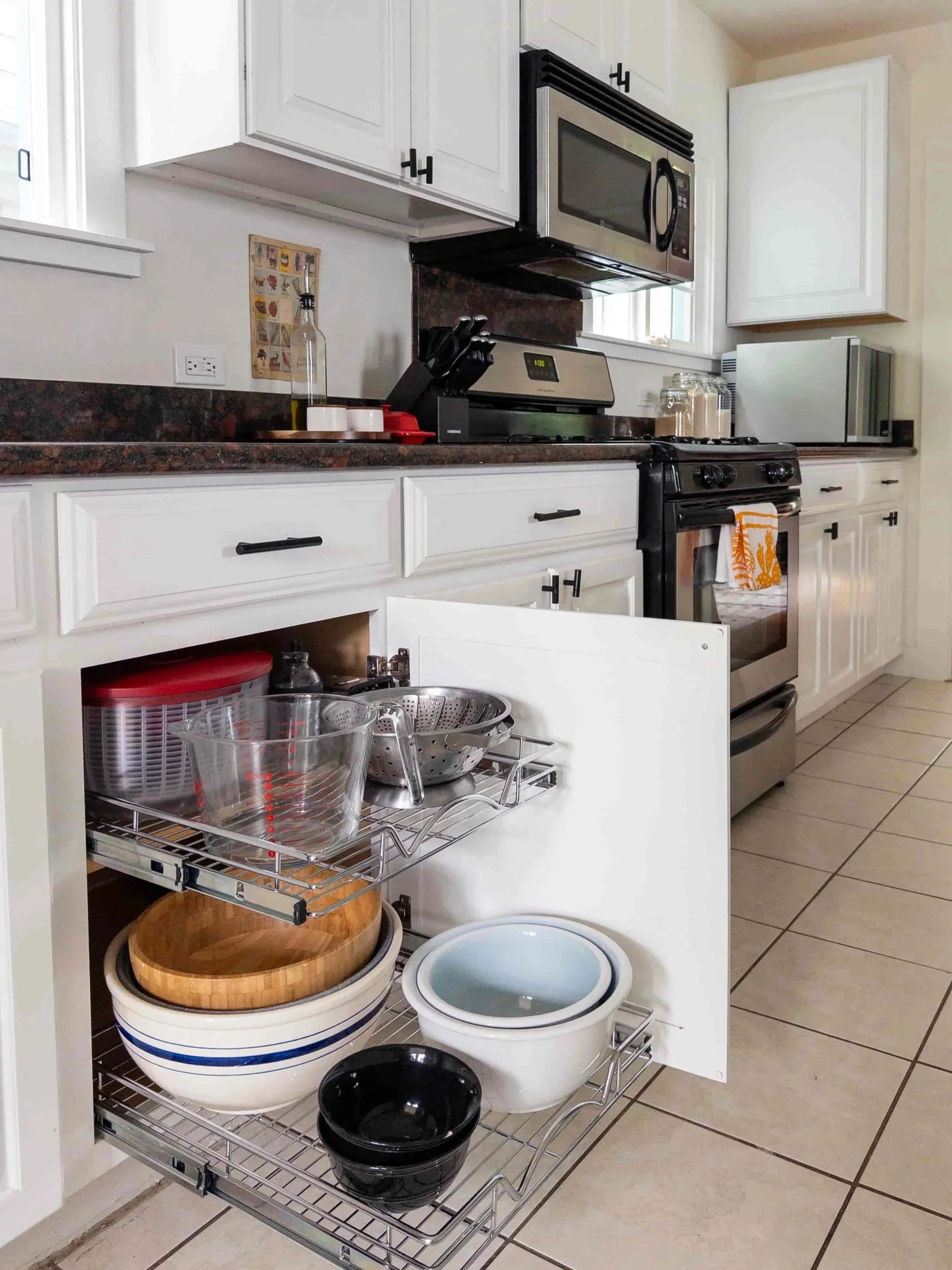 Open kitchen cabinet with dishes, bowls, and kitchenware organized on wire shelves inside cabinet, with tiled floor and white cabinets.