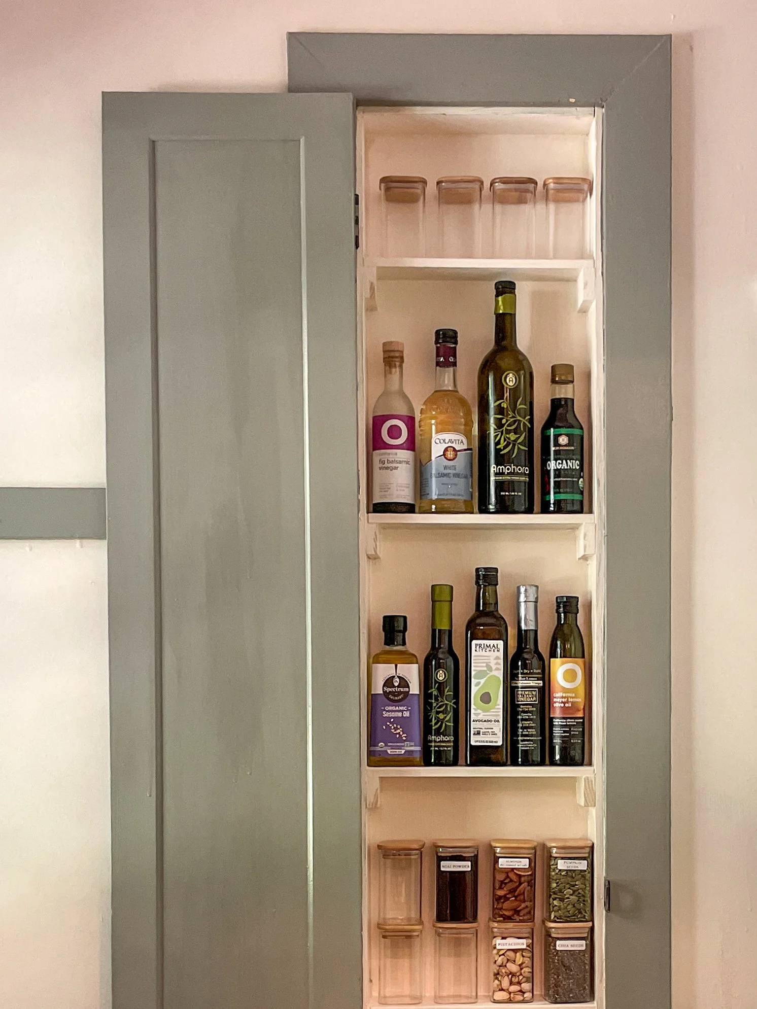A wooden spice rack filled with various bottles, jars, and containers of spices and cooking ingredients, positioned next to a closed gray cabinet.