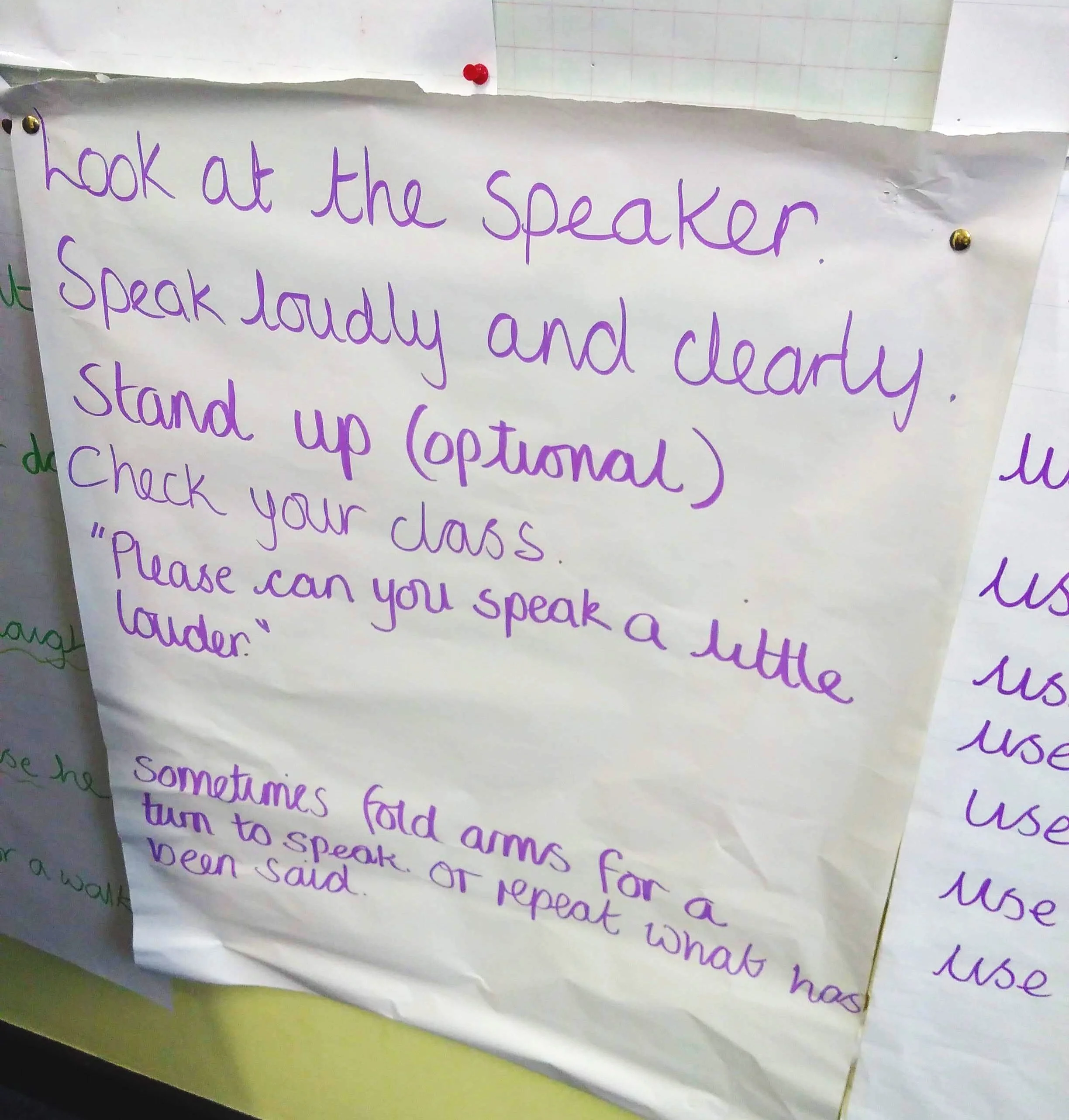 A handwritten poster with a list of guidelines: Look at the speaker. Speak loudly and clearly. Stand up (optional). Check your class. "Please can you speak a little louder?" Sometimes fold arms for a turn to speak or repeat what has been said.