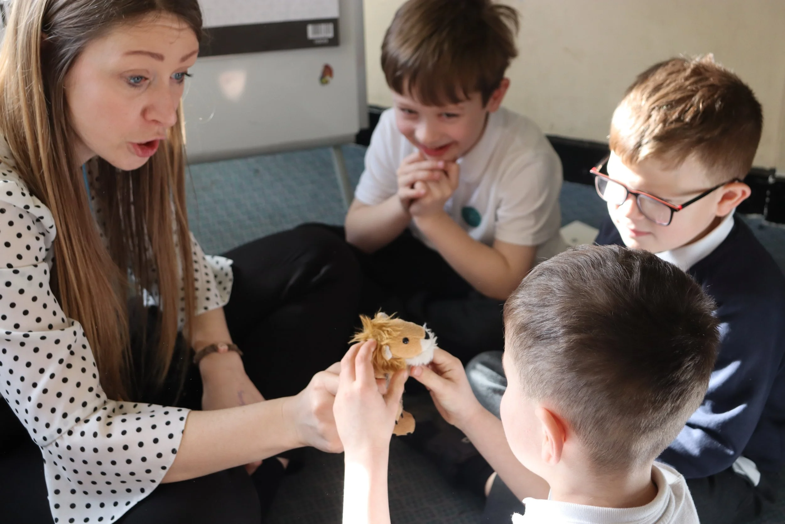 A teacher passing a soft toy to a pupil while two others observe
