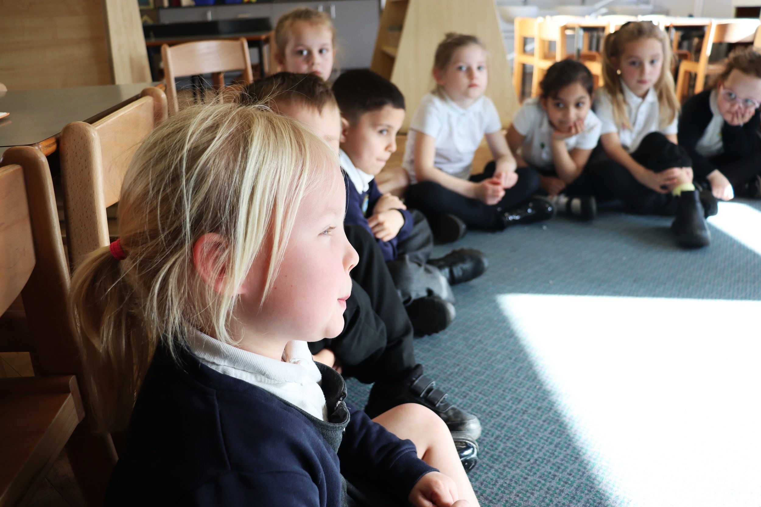 Children sitting on the floor in a circle; one speaks while the others listen attentively