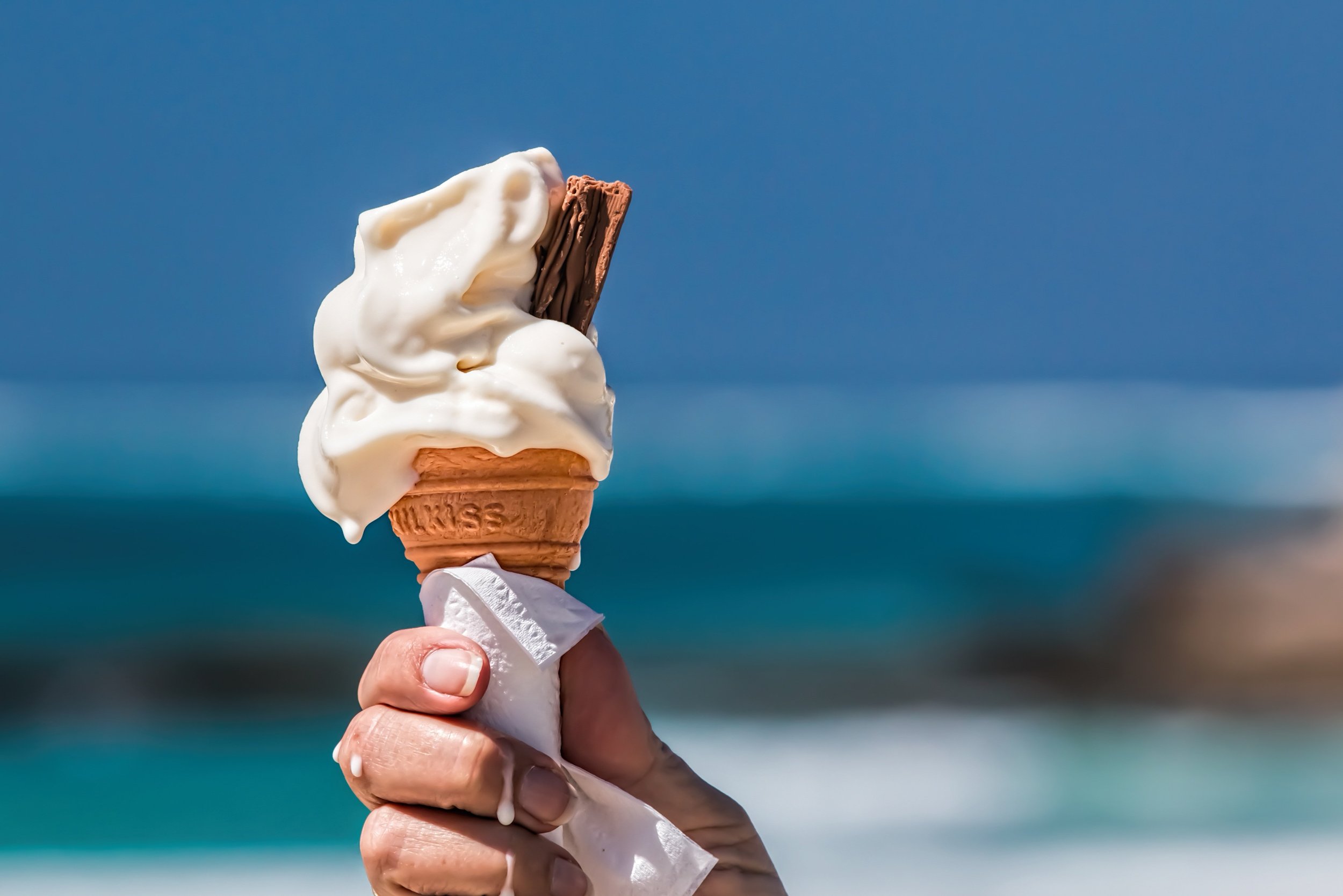 A hand holding an ice cream with blue sky behind