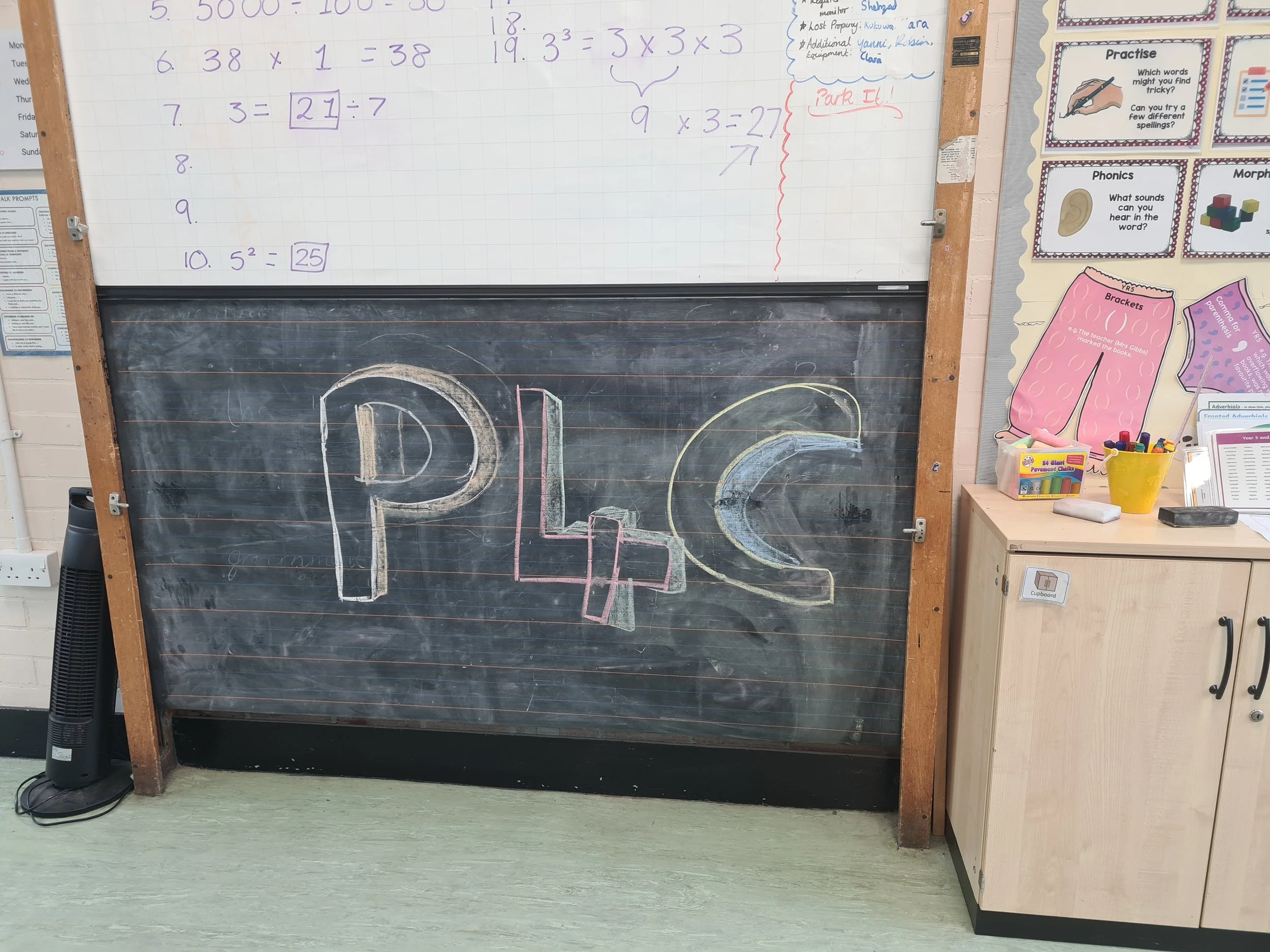 'P4C' drawn in coloured chalk on a classroom chalkboard, with other classroom stuff around