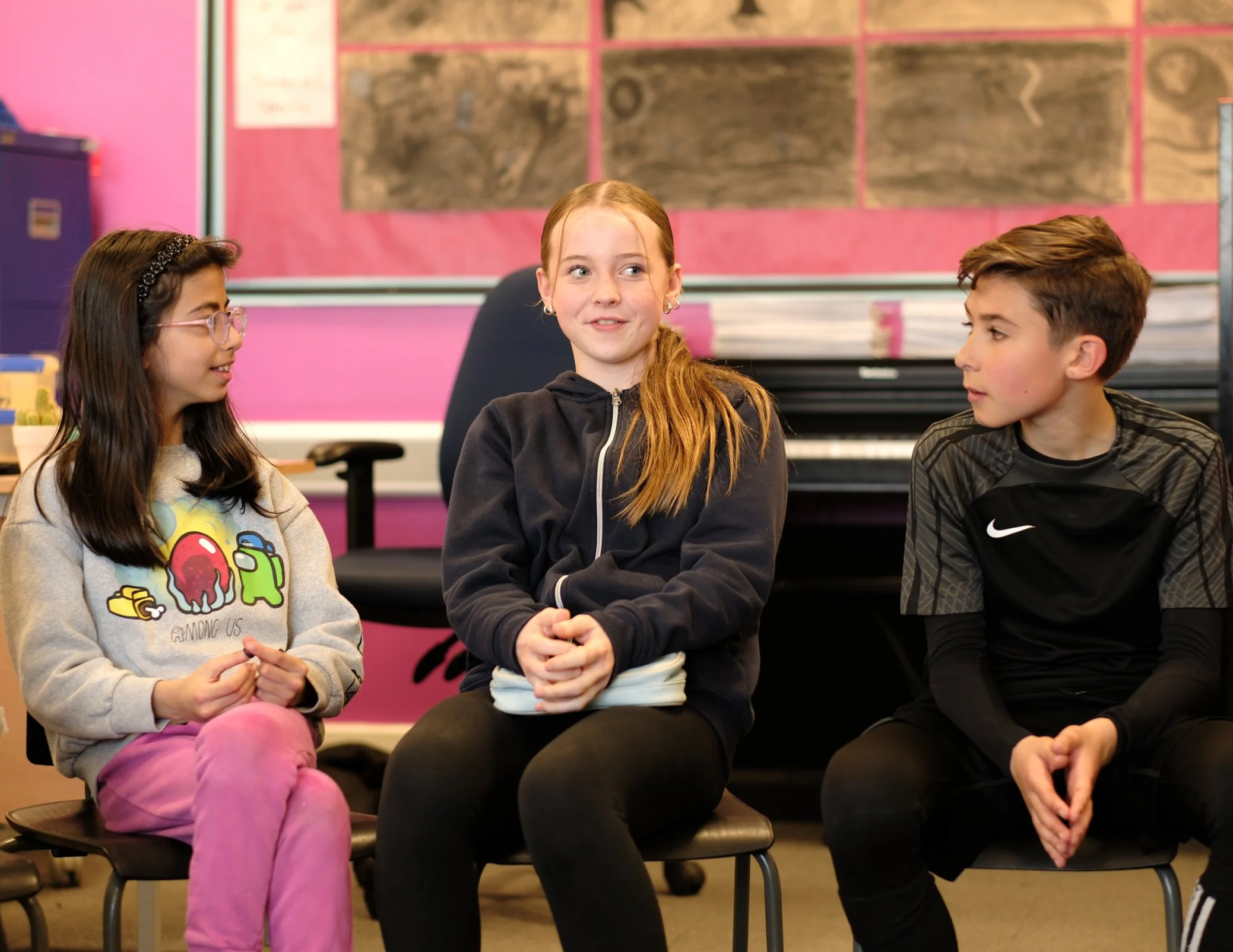 three pupils on chairs, one speaking, two paying attention
