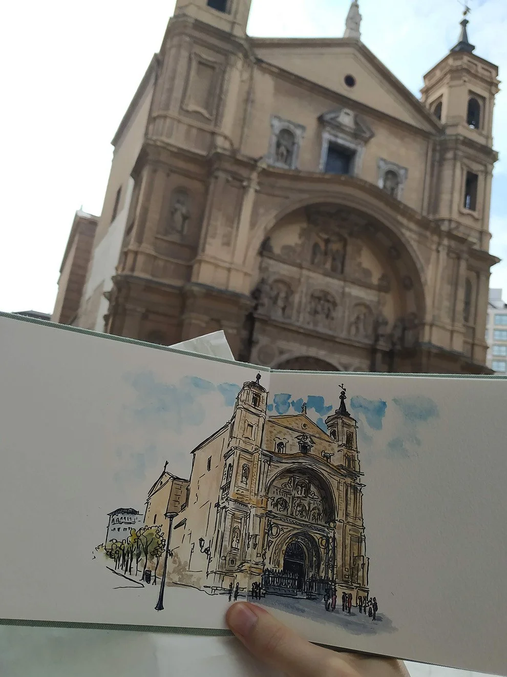 Dibujo de una iglesia en primer plano y una iglesia real en segundo plano, vista desde abajo, en un día despejado.