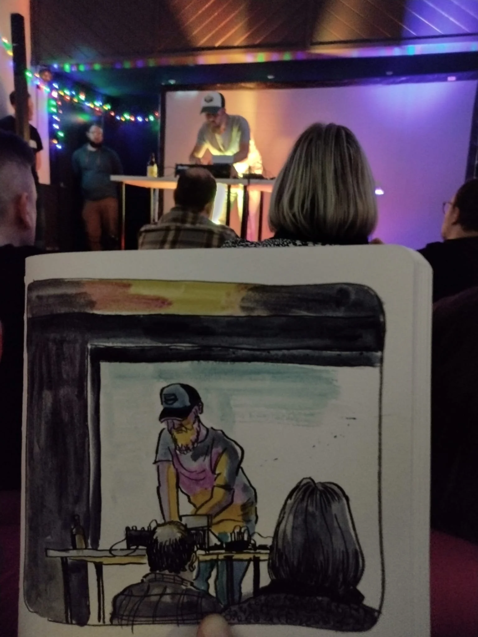 Una ilustración de un DJ tocando en un escenario con tres espectadores frente a él, en un ambiente con luces decorativas de colores.