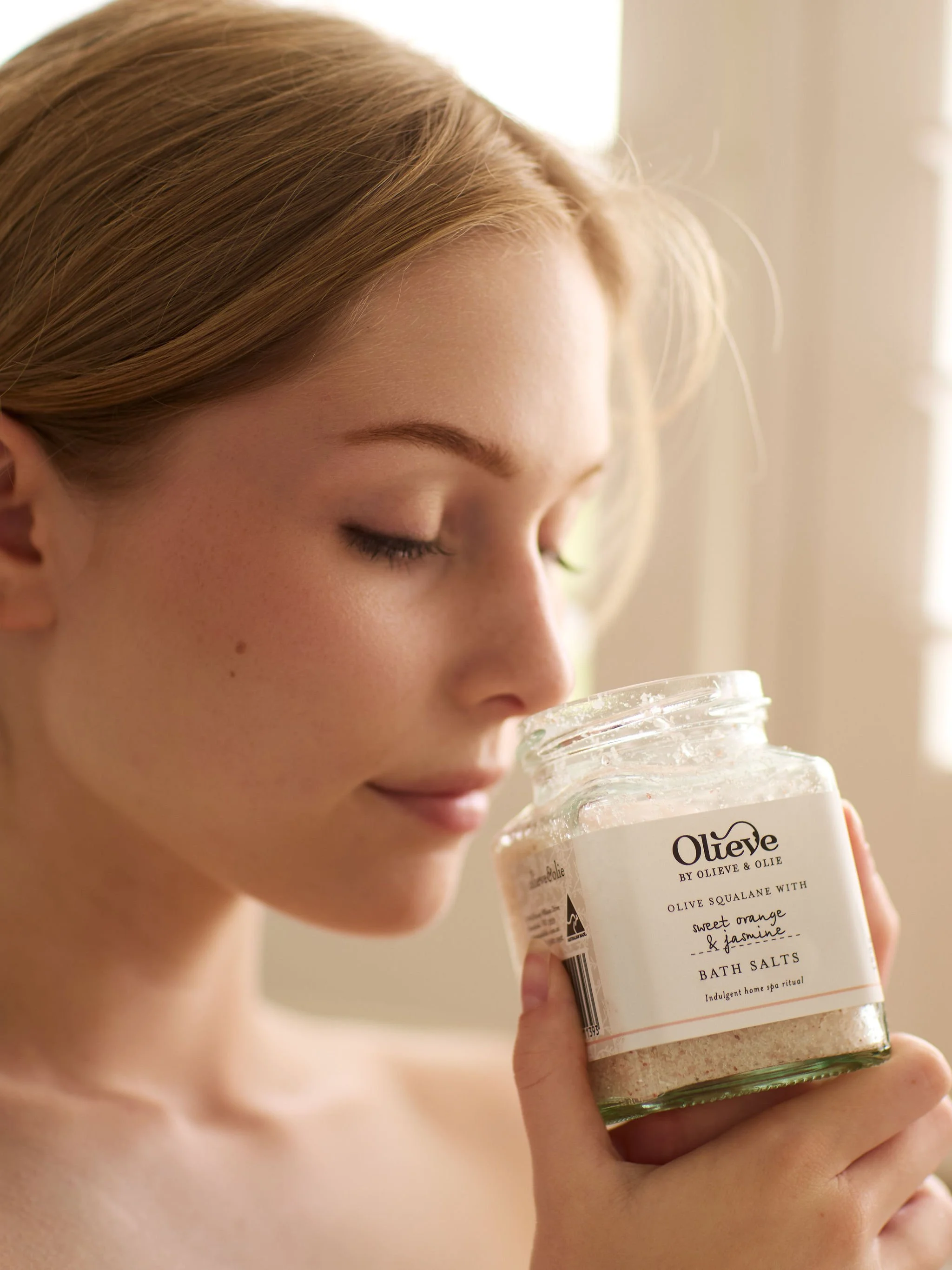 women smelling a glass jar of Bath Salts.