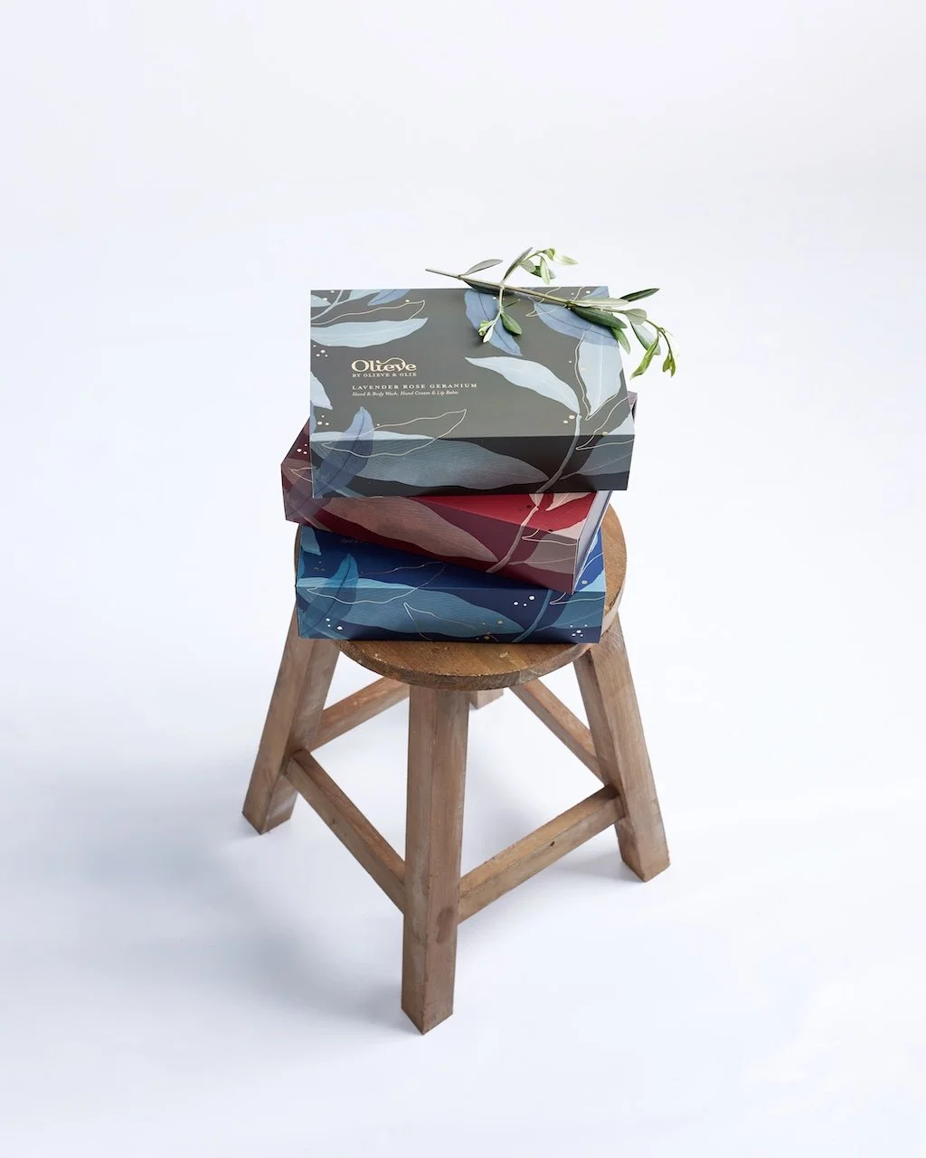 3 gift boxes sit on a wooden stool with a decorative small branch of olive leaves on top
