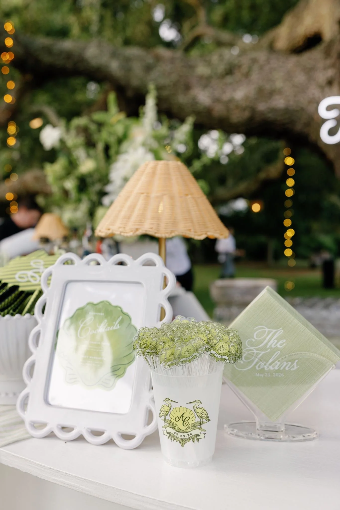 Table setup with personalized party favors, a small paper umbrella, and decorative cards with initials and date, indicating a wedding celebration.