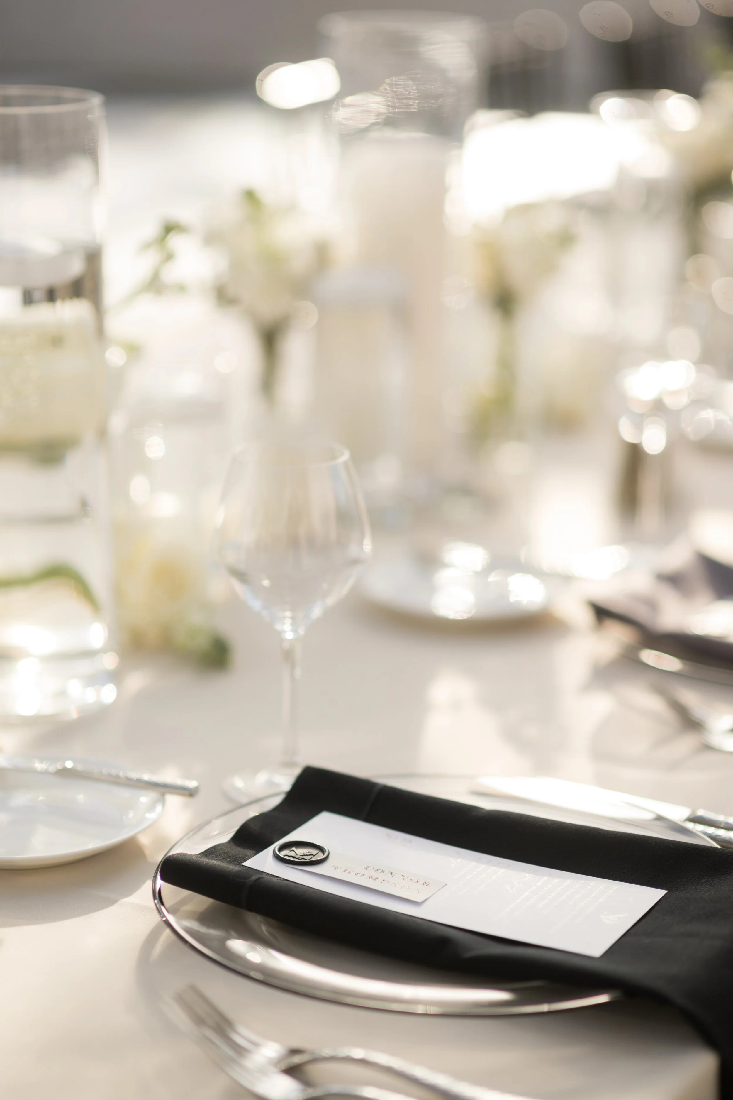 A table with empty wine glasses, a menu on a silver tray, and soft sunlight.