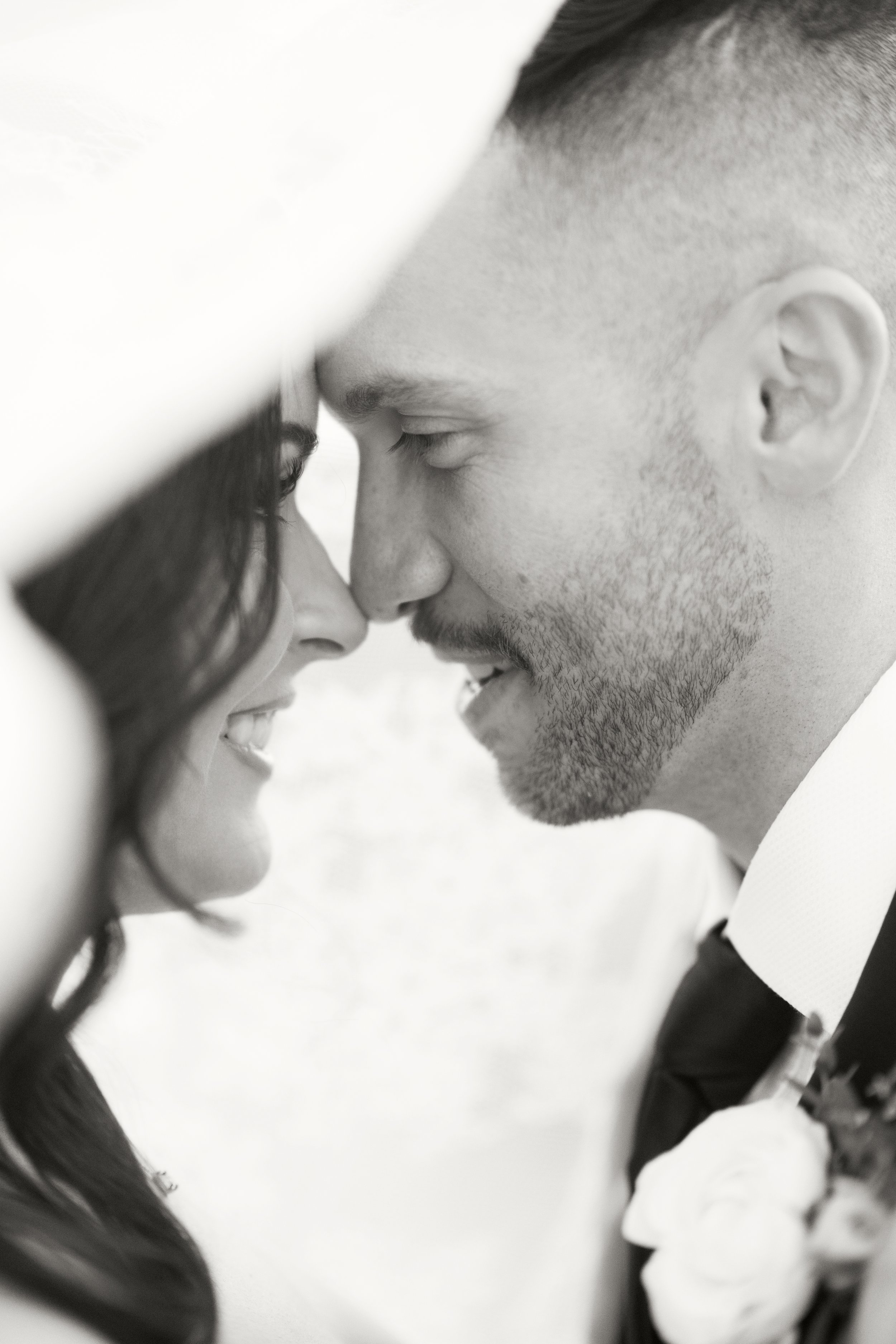 A close-up black and white photo of a man and woman leaning their foreheads and noses together, eyes closed, in a tender moment.