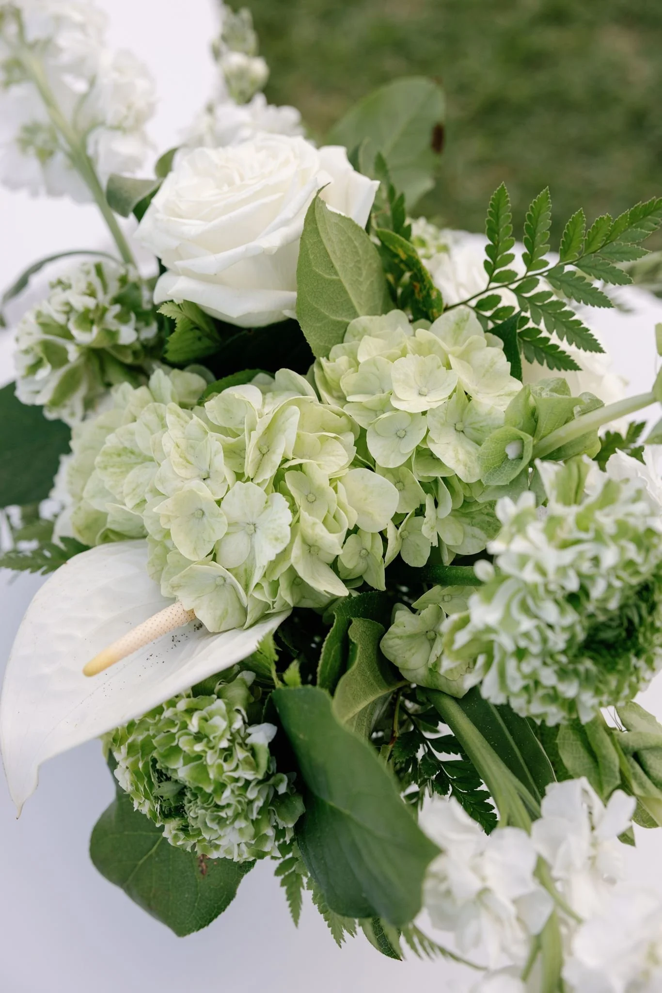 Close-up of a white floral arrangement with roses, hydrangeas, anthurium, and assorted greenery.