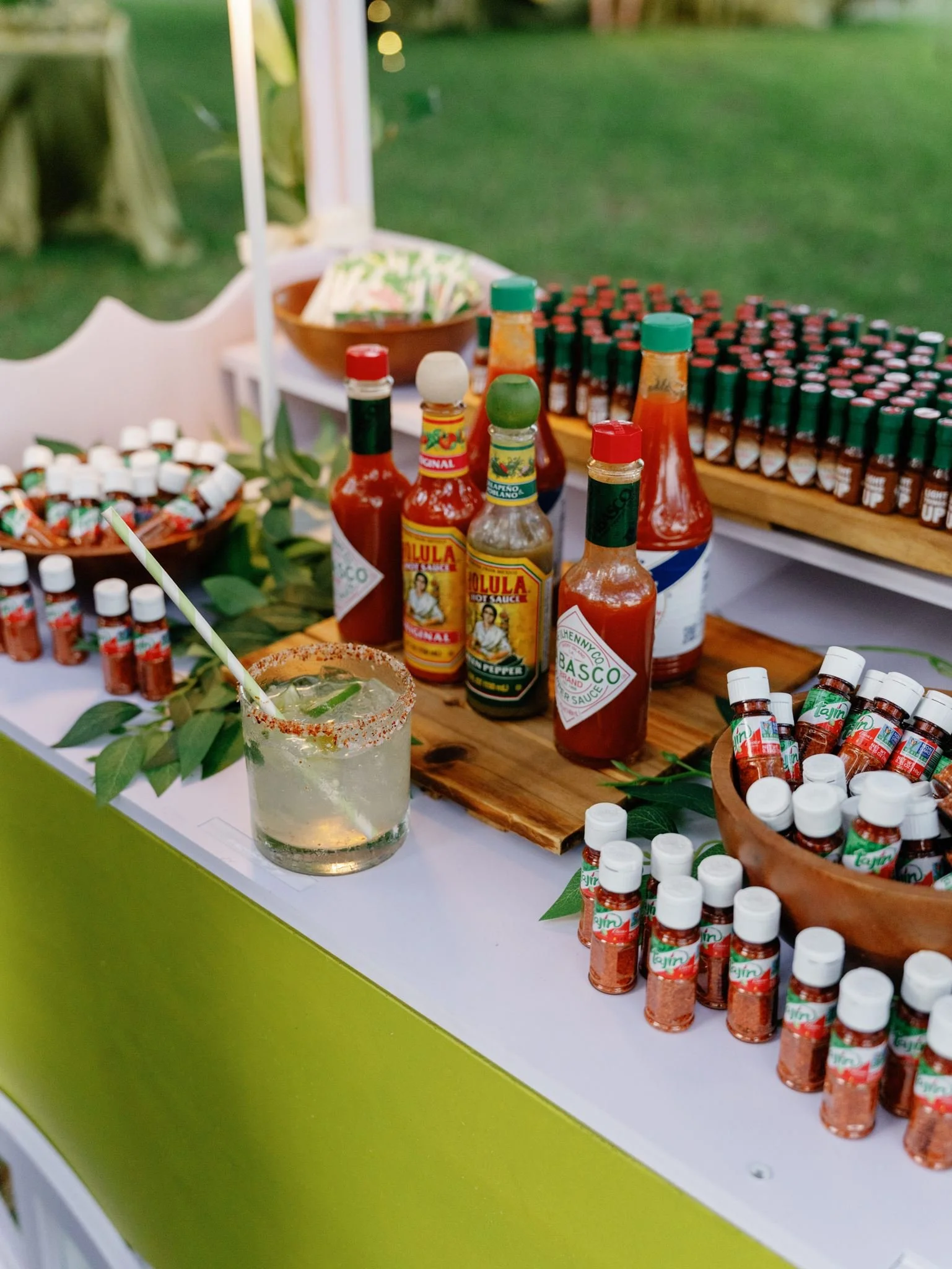 A display of various hot sauce bottles, small spice bottles, and a jar of chili powder on a table with a green and white background.