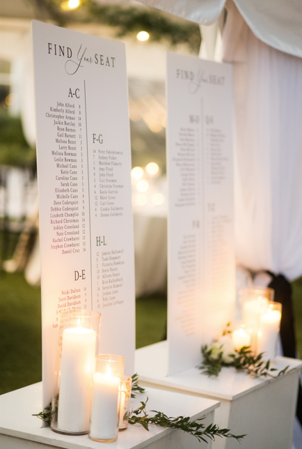 Wedding seating chart with candles and greenery at an outdoor reception.