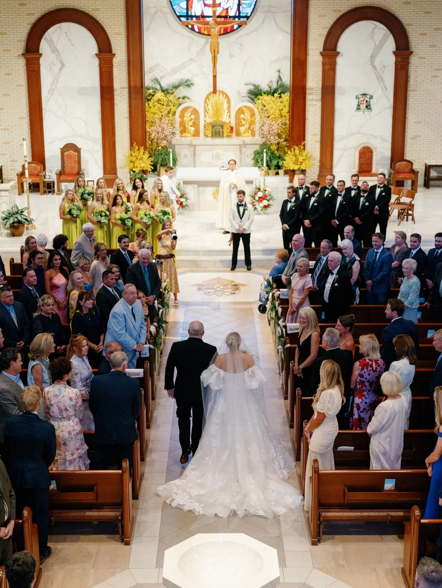 A bride and groom walk down the aisle in a church after their wedding ceremony, with guests standing and watching.