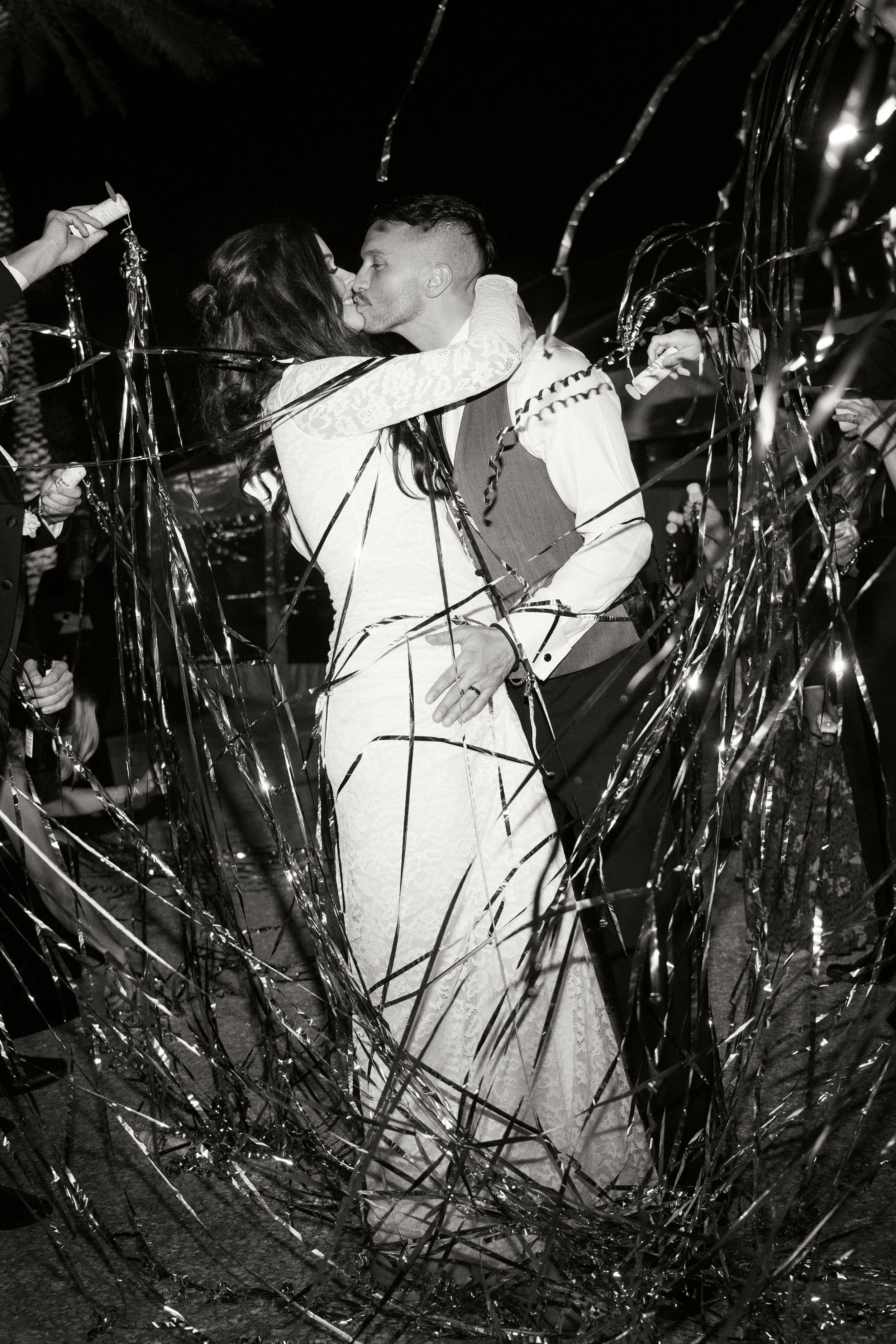 A couple is kissing at a celebration, surrounded by metallic streamers and confetti.