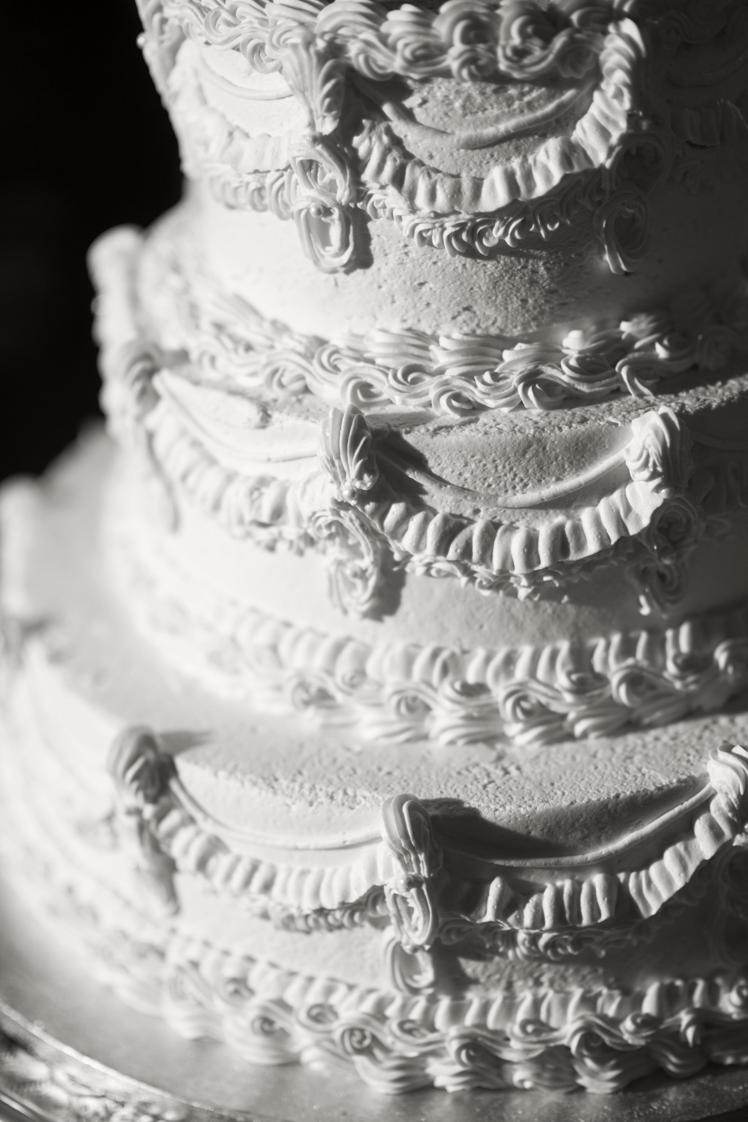A close-up of a multi-tiered wedding cake decorated with white icing and intricate piping details.