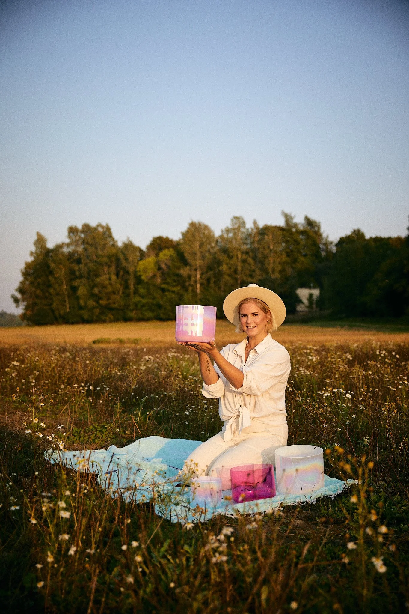 Woman sitting in a sunlit field with wrapped gifts and sound healing instruments, representing Module 1: Sound of the certification
