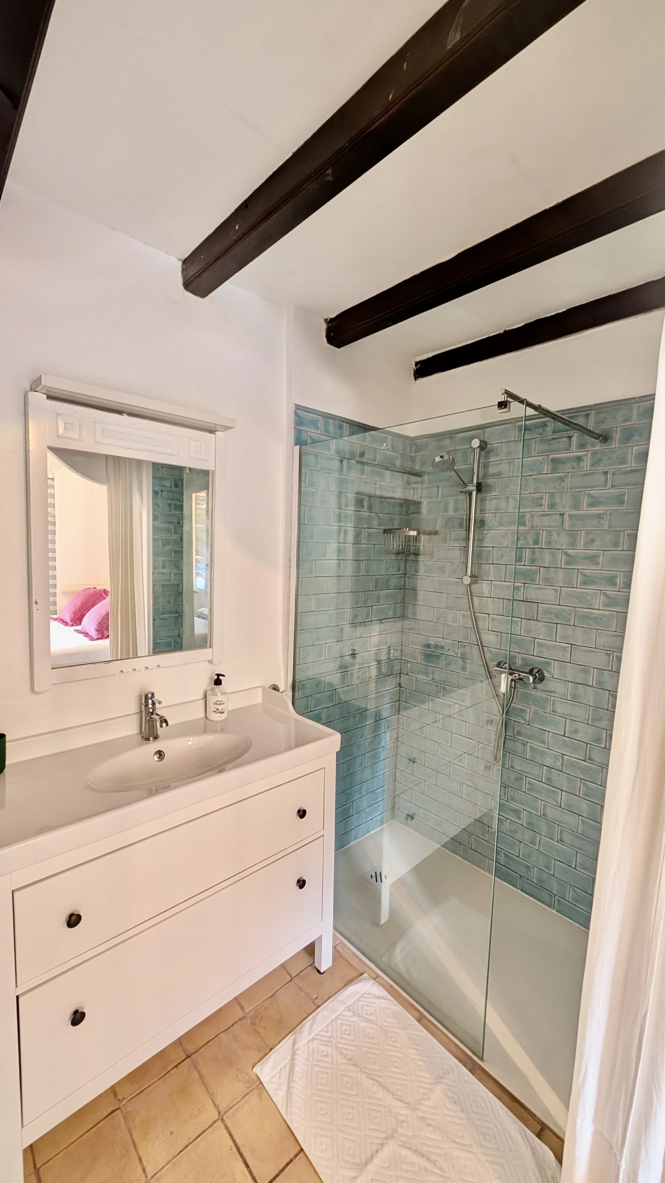 Bathroom with a white vanity, mirror, soap dispenser, and a glass-enclosed shower with blue-green subway tiles.