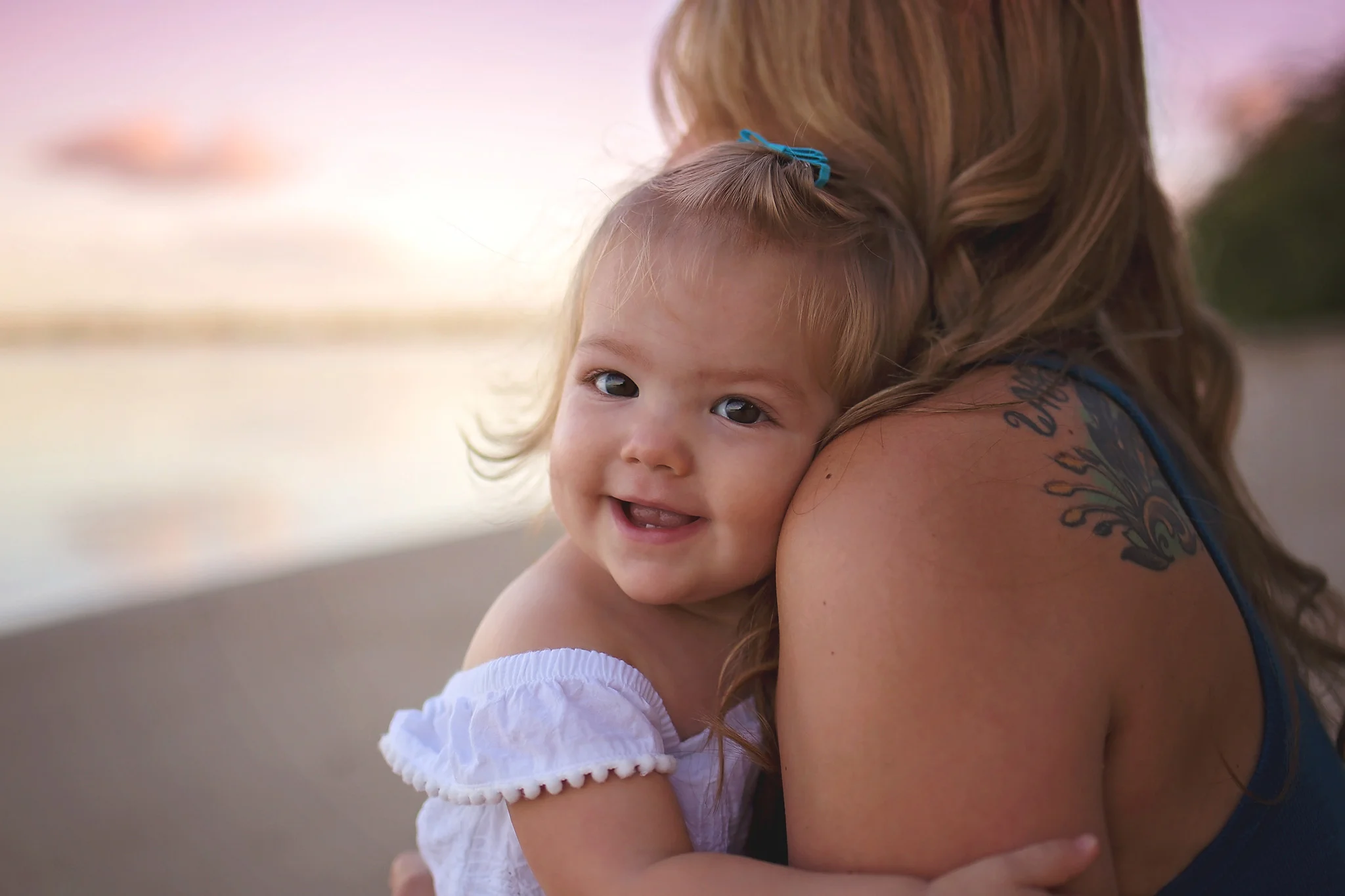 Little girl smiling holding on to mom while sitting at Dog Beach on Hickam AFB in Honolulu, Hawaii.