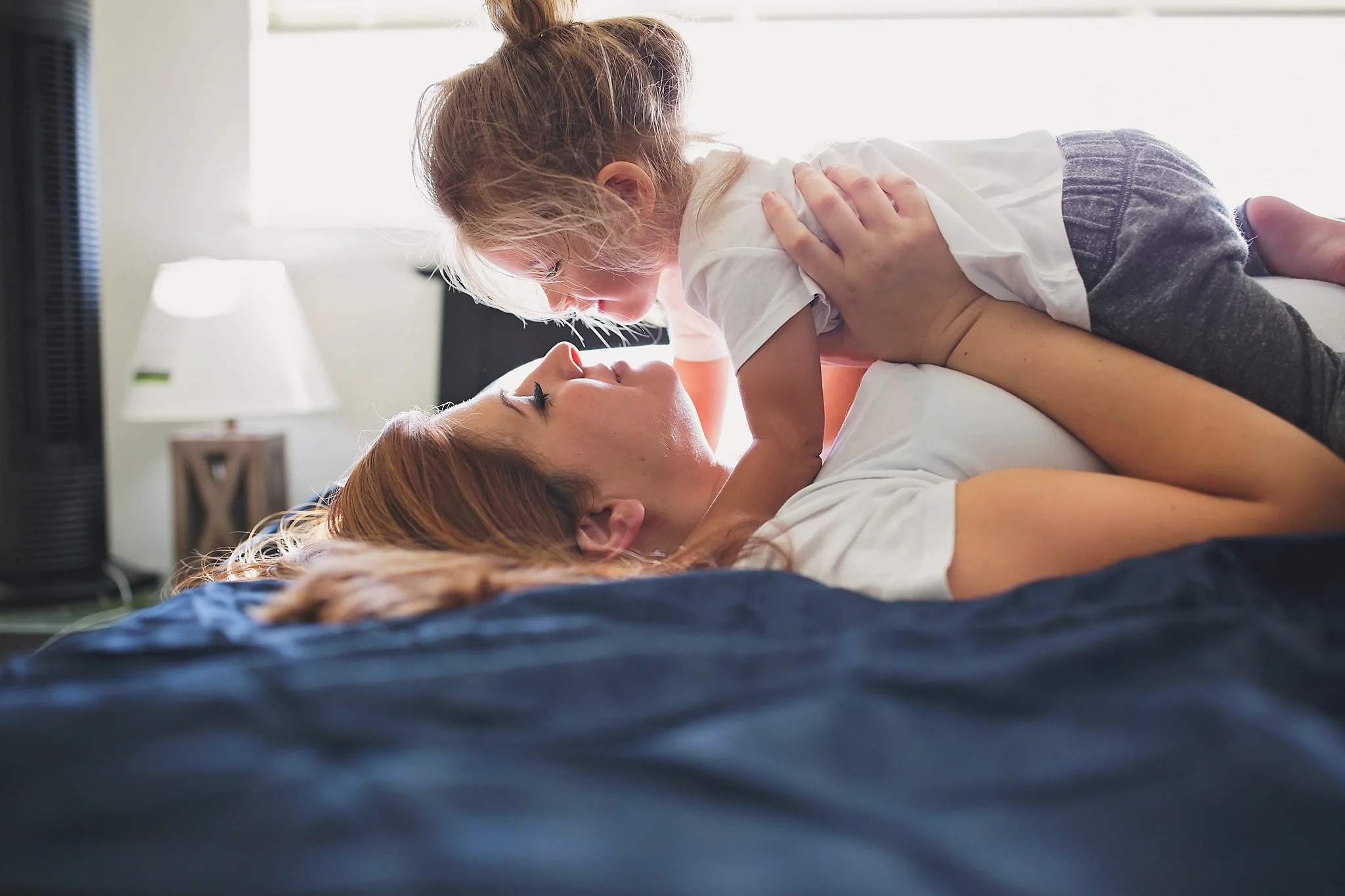 Toddler laying on top of Mom while looking into each other eyes durning an in-home maternity session.