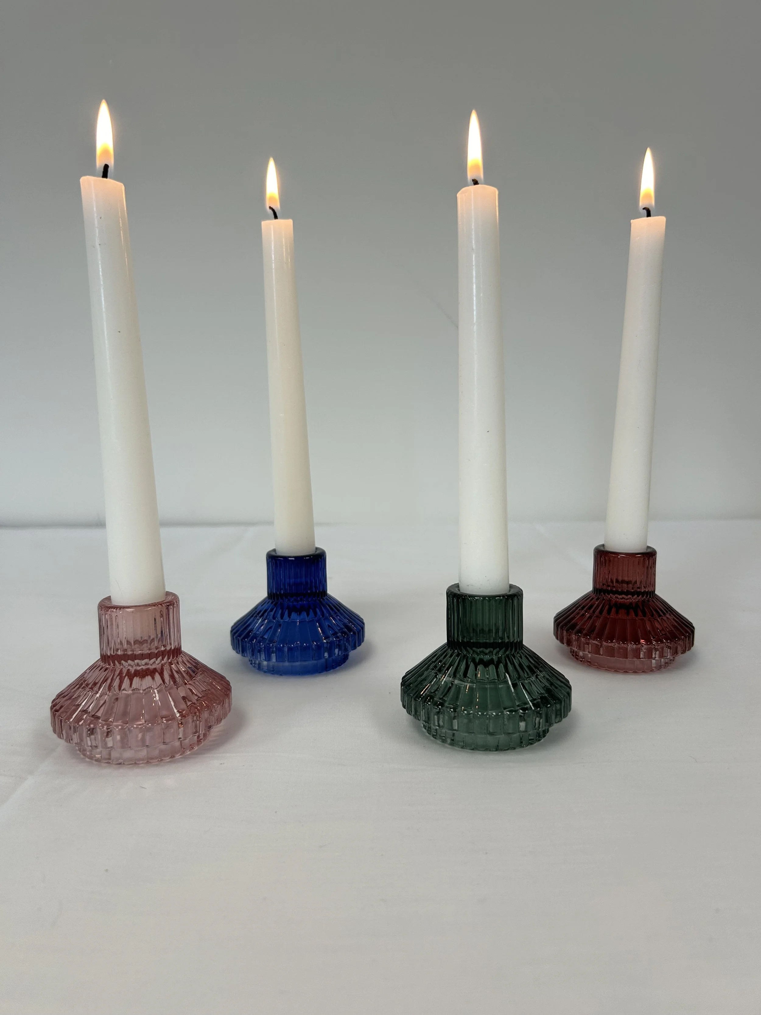 Four short, colourful candle holders with white candlesticks burning