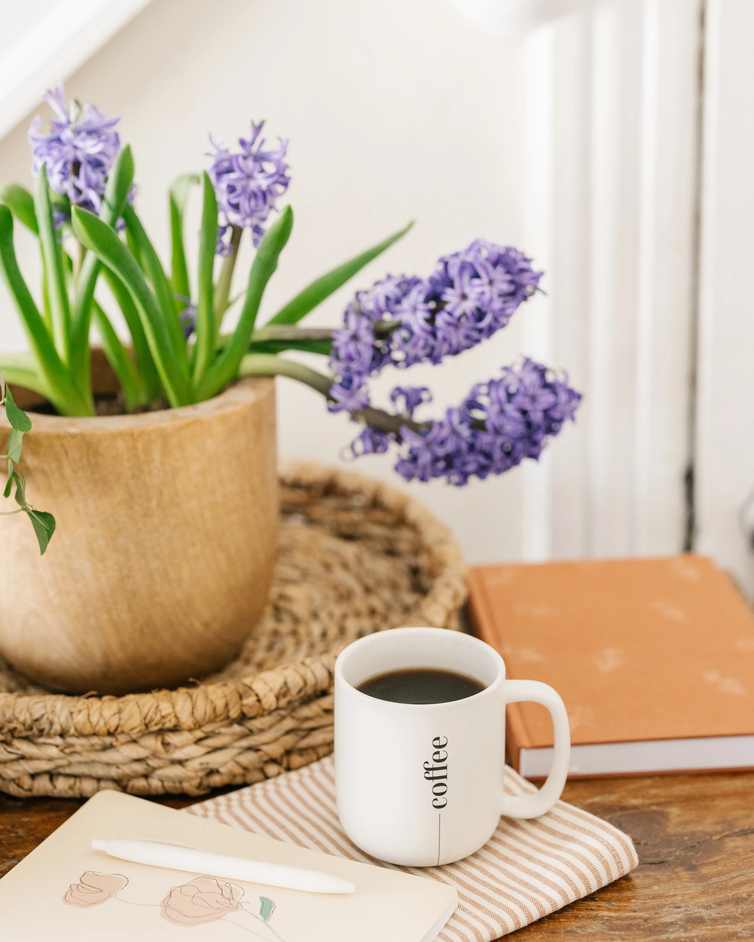 Mug of coffee on a stack on journals with a purple hyacinth in bloom