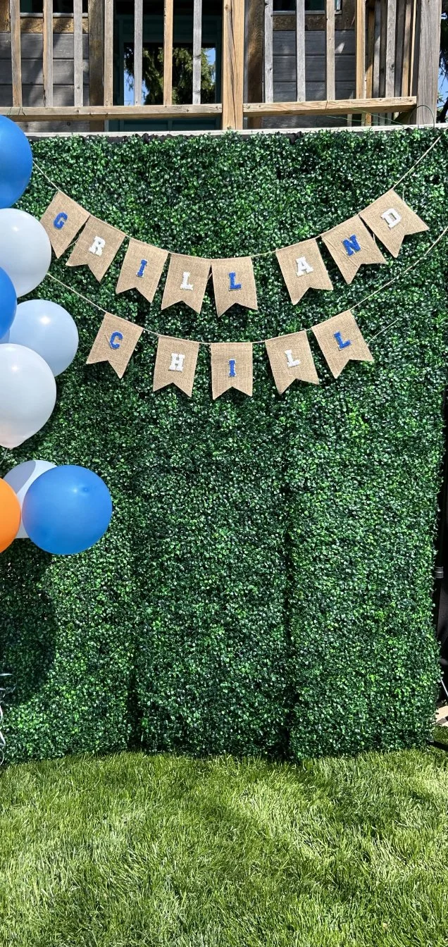 Boxwood backdrop with bunting reading "Grill and Chill" with balloons on the side