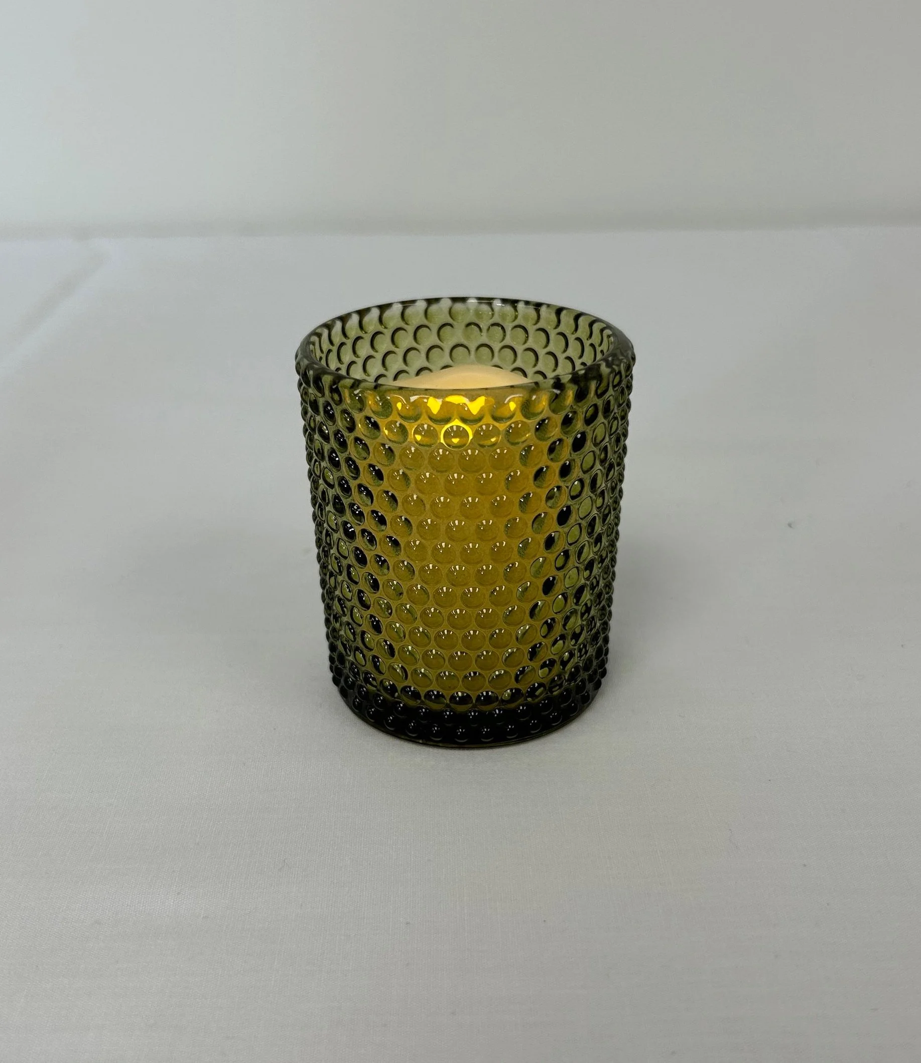 Vintage mossy green glass votive with short candle illuminated inside