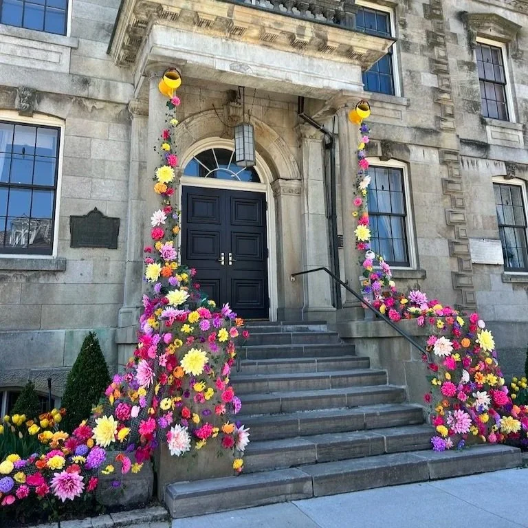 The courthouse in downtown Niagara-on-the-Lake adorned with yellow watering cans on each pillar with flowers cascading from them to the ground