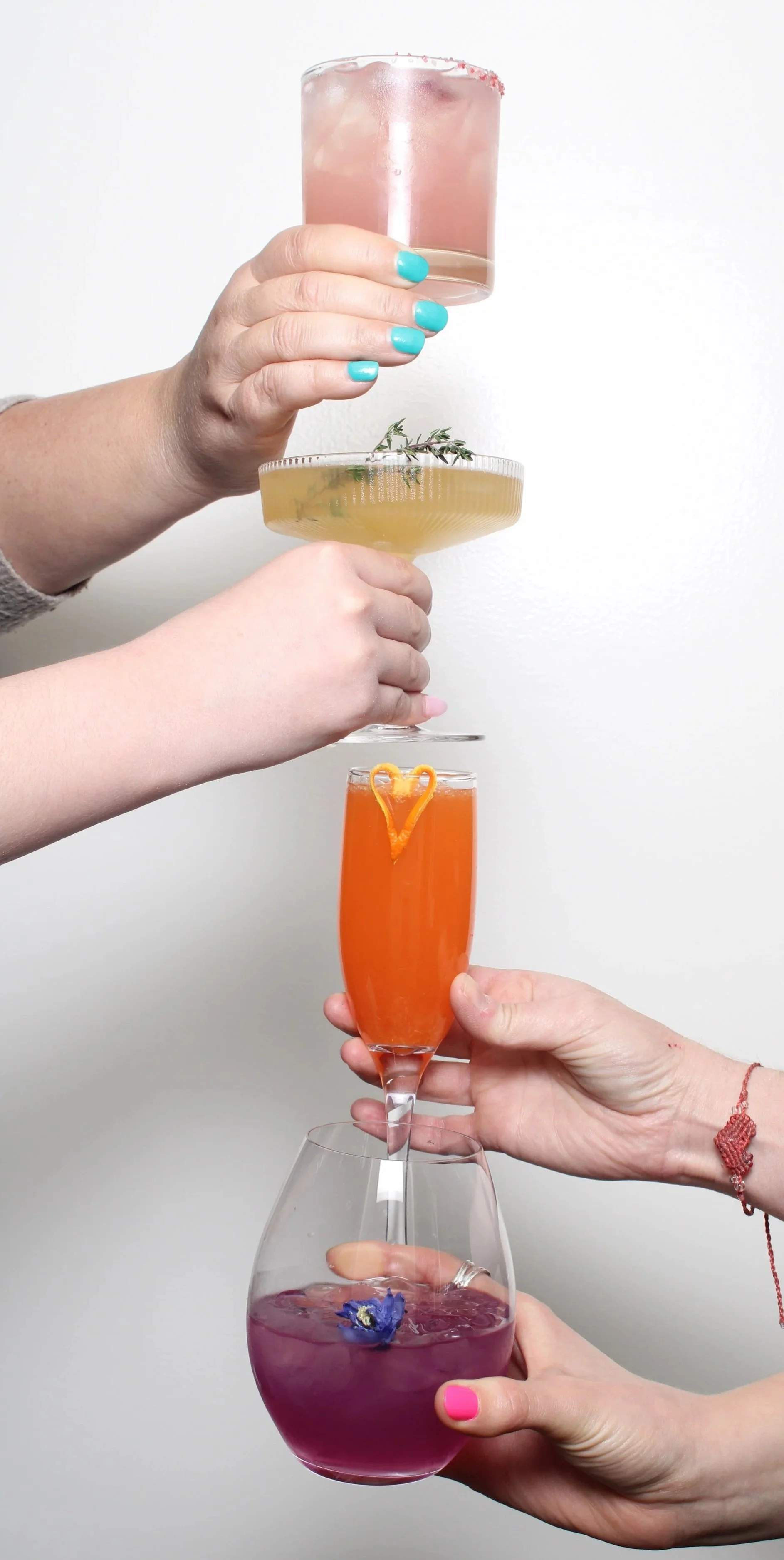 Four cocktails being held in a vertical line against a white wall