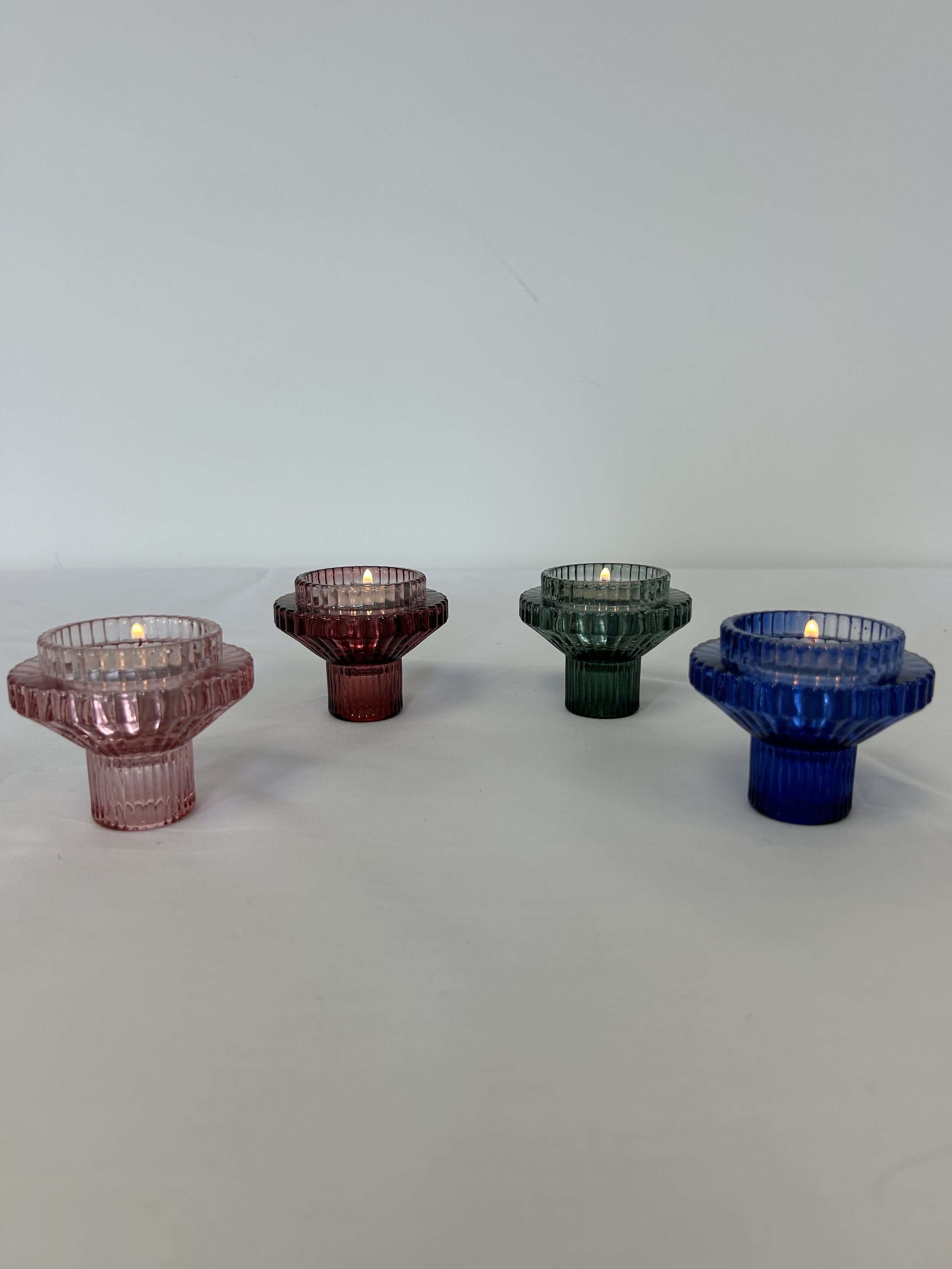 Four short, colourful candle holders with tea lights burning