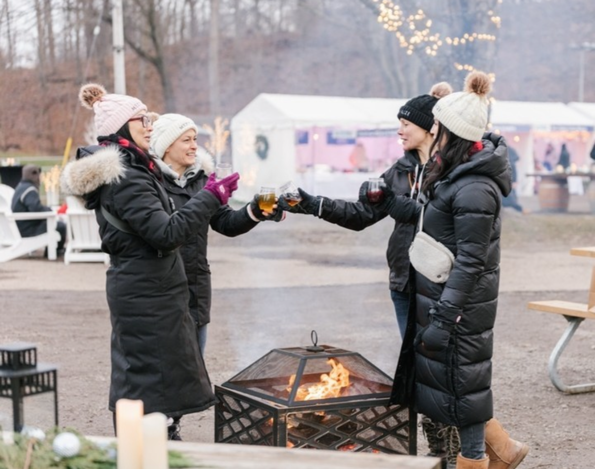 Four women cheers-ing over a fire pit at the Twenty Valley Winter Wine Fest