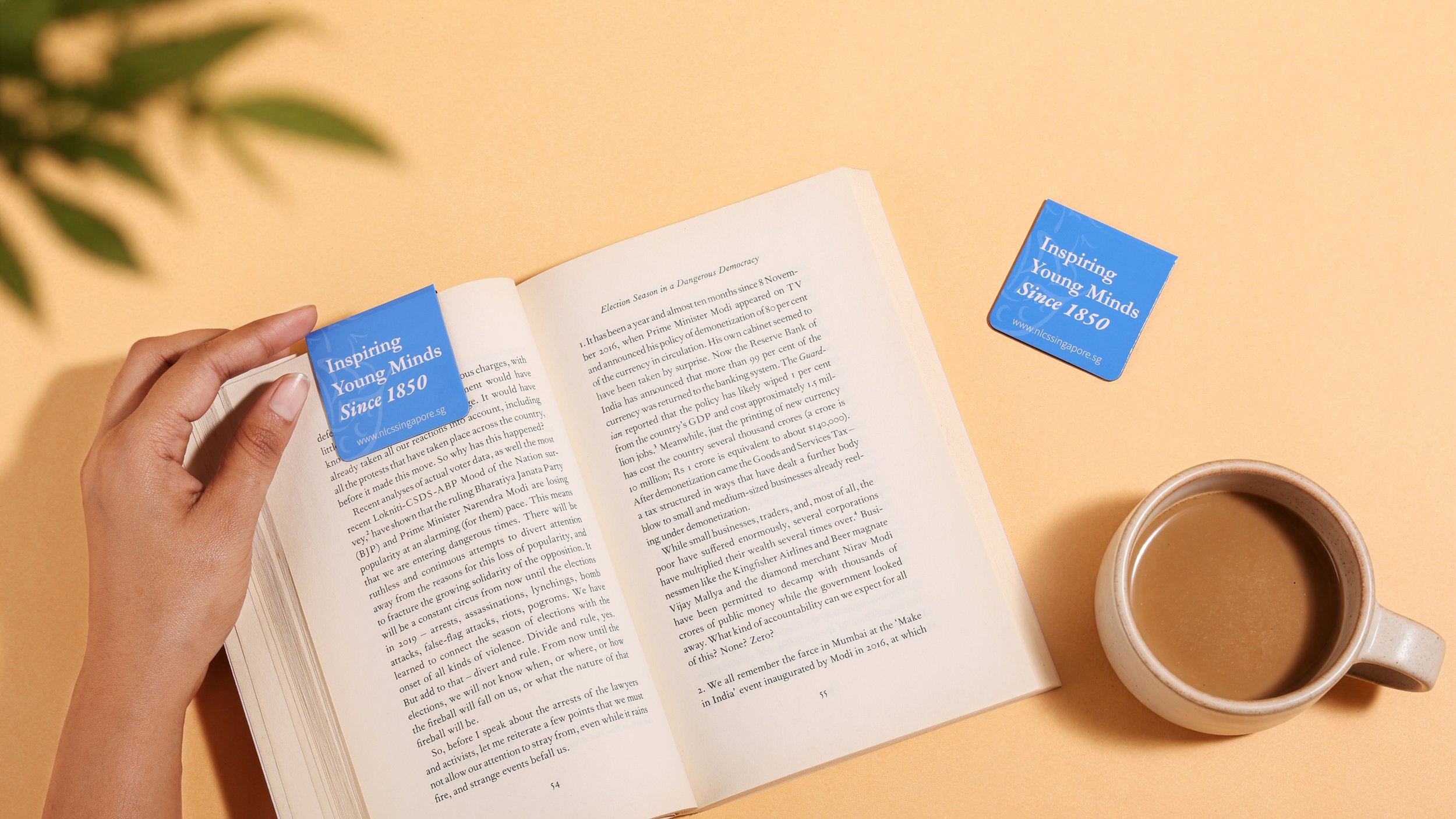 Custom magnet bookmark clip with NLCS Singapore school branding, blue printed page marker clipped onto a book