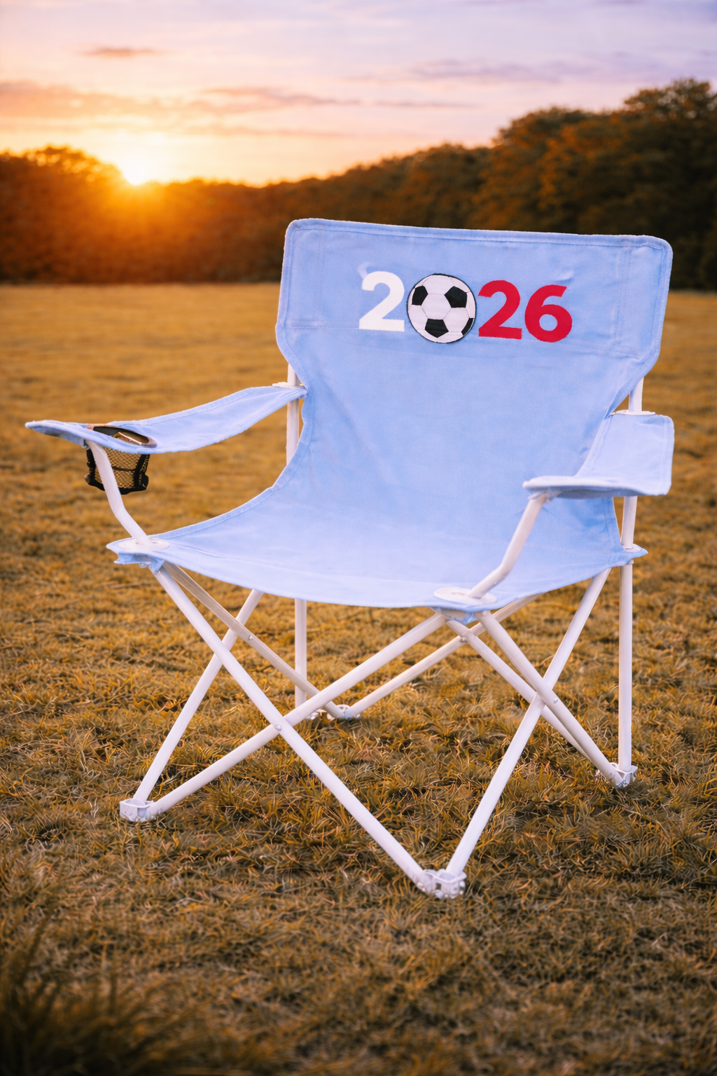Light Blue custom chair with arm rest and cup holder and  2026 written on it with 0 being  a football placed on grass with sunset in background