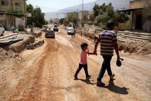 A father and his daughter cross a street under renovations as part of a U.S. aid grant in the village of al-Badhan, north of Nablus in Israeli occupied West Bank in August 2018. JAAFAR ASHTIYEH / AFP/GETTY IMAGES