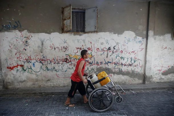 Mohammad Nimnim wheels water jugs, to fill at the mosque at Beach refugee camp. (Photo: Abdel Kareem Hanna)