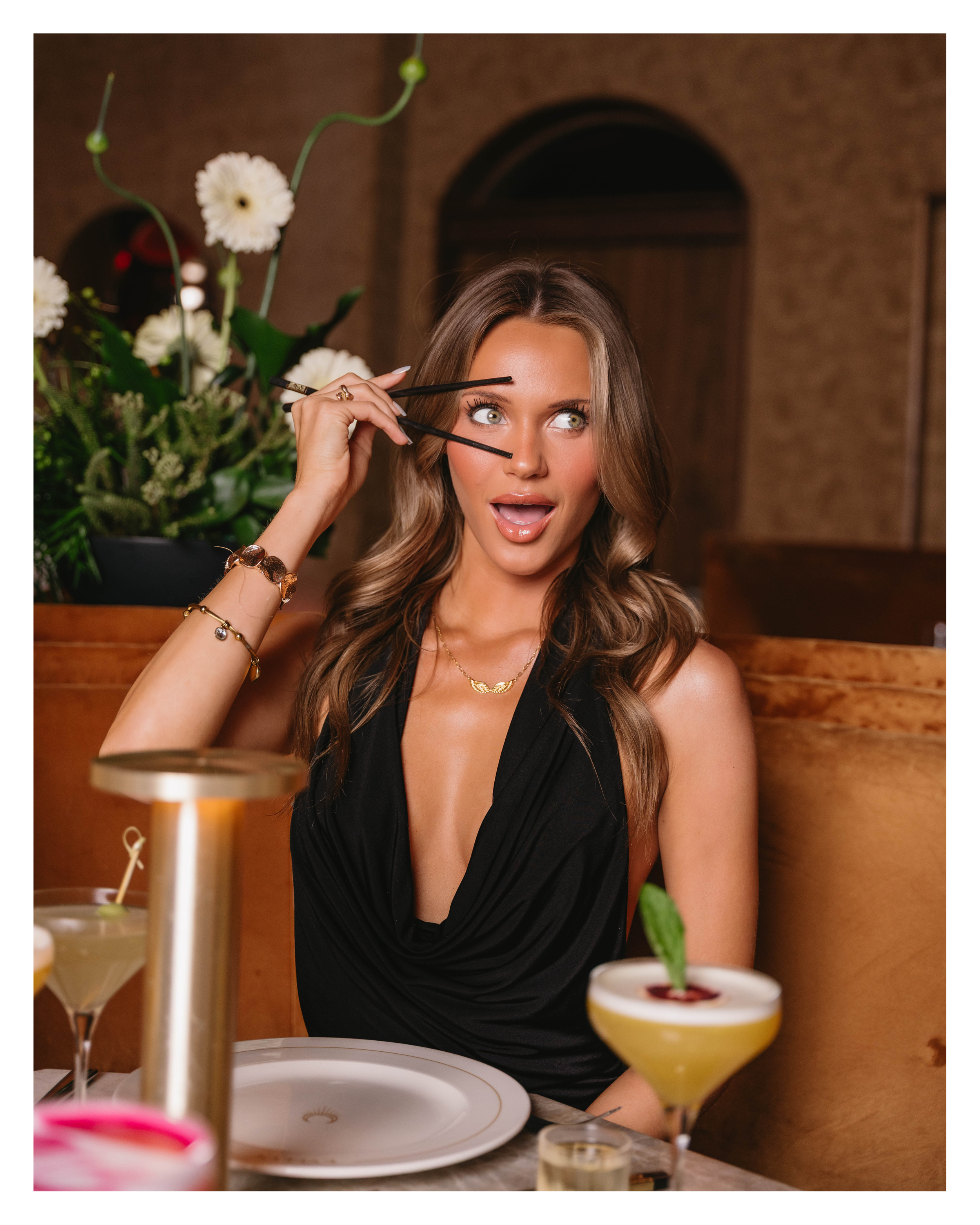 Portrait of a guest with chopsticks and cocktails in a velvet booth at EVELYN in the Dallas Design District