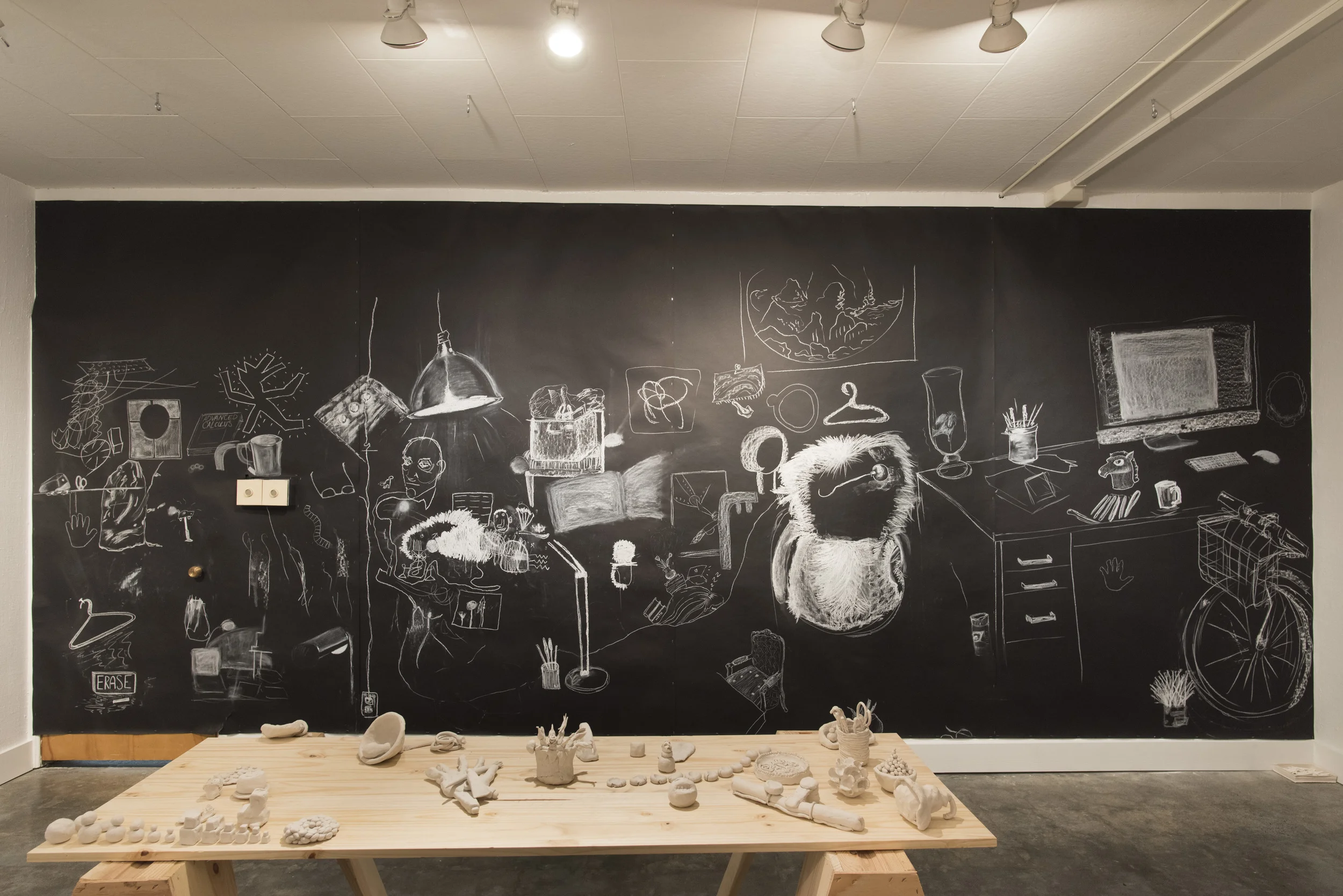 parlor games: parallax (installation detail showing participatory wall drawing) In response to a call, artists and scientists from around the world contributed over 80 snapshot photographs of their workspaces. Photos are hung on the wall and scattered on the makeshift worktable for browsing. Participants drew selected objects from the photos on the wall, while other participants made clay objects based on the drawings. 