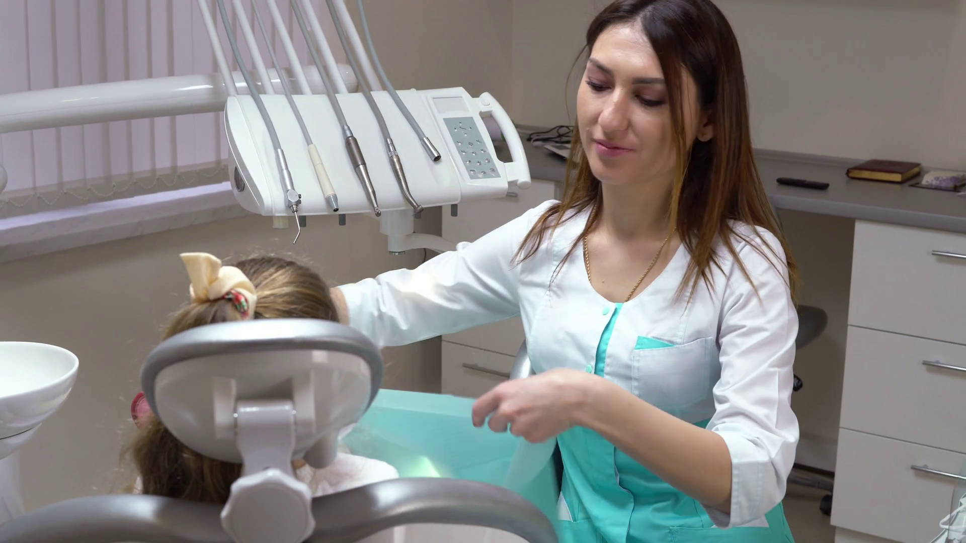videoblocks-friendly-female-dentist-putting-a-napkin-on-the-cute-little-girl-taking-on-gloves-and-protective-glasses-before-doing-routine-check-up-shot-in-4k_sjgub2qs6x_thumbnail-full01.png